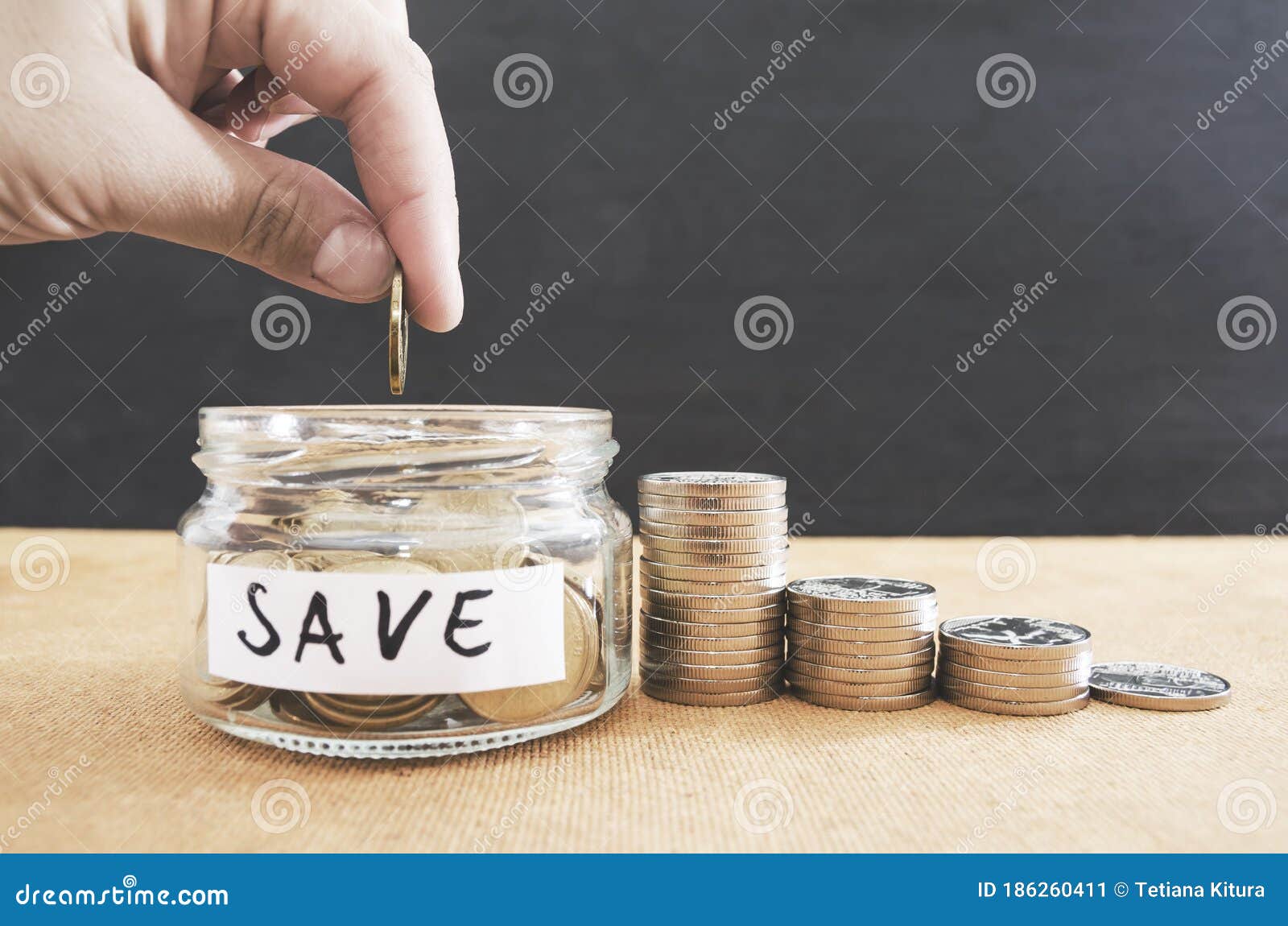 woman hand is putting a coin in a glass bottle and a pile of coins on a brown wooden table,investment business, retirement, finan