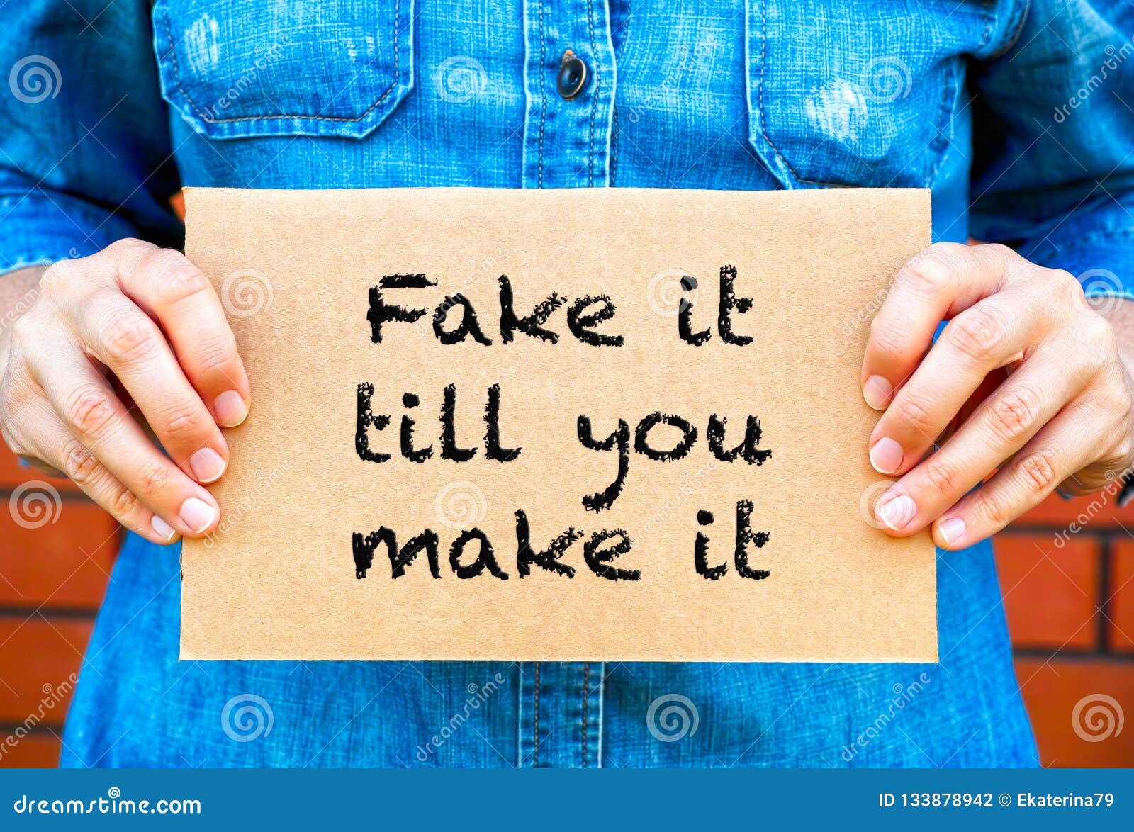 woman hands holding piece of cardboard with phrase fake it till