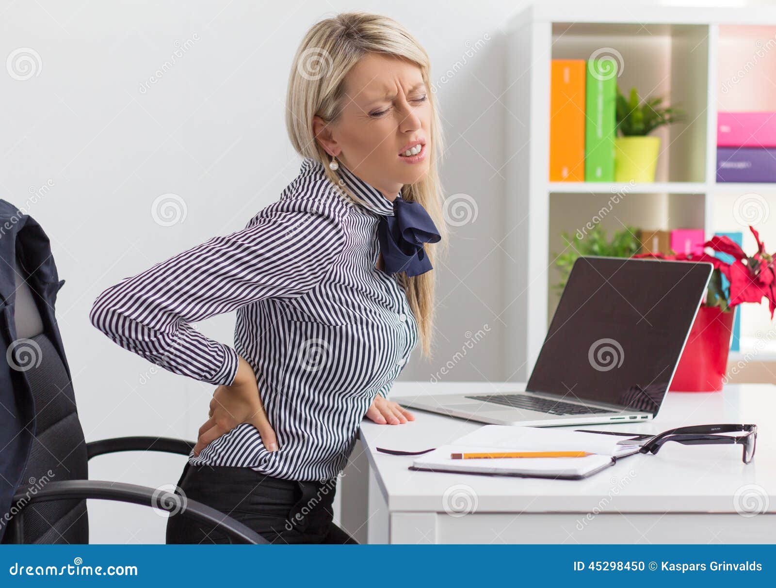 woman having back pain while sitting at desk in office