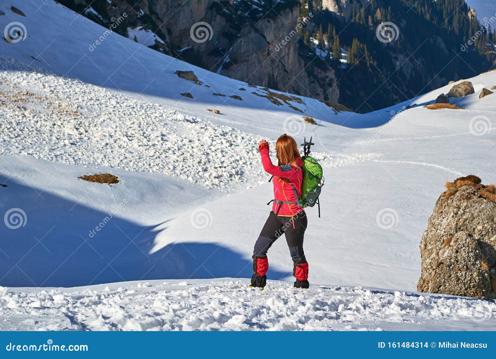 woman hiker looking back towards a recent wet snow avalanche, in malaiesti valley, bucegi mountains, romania