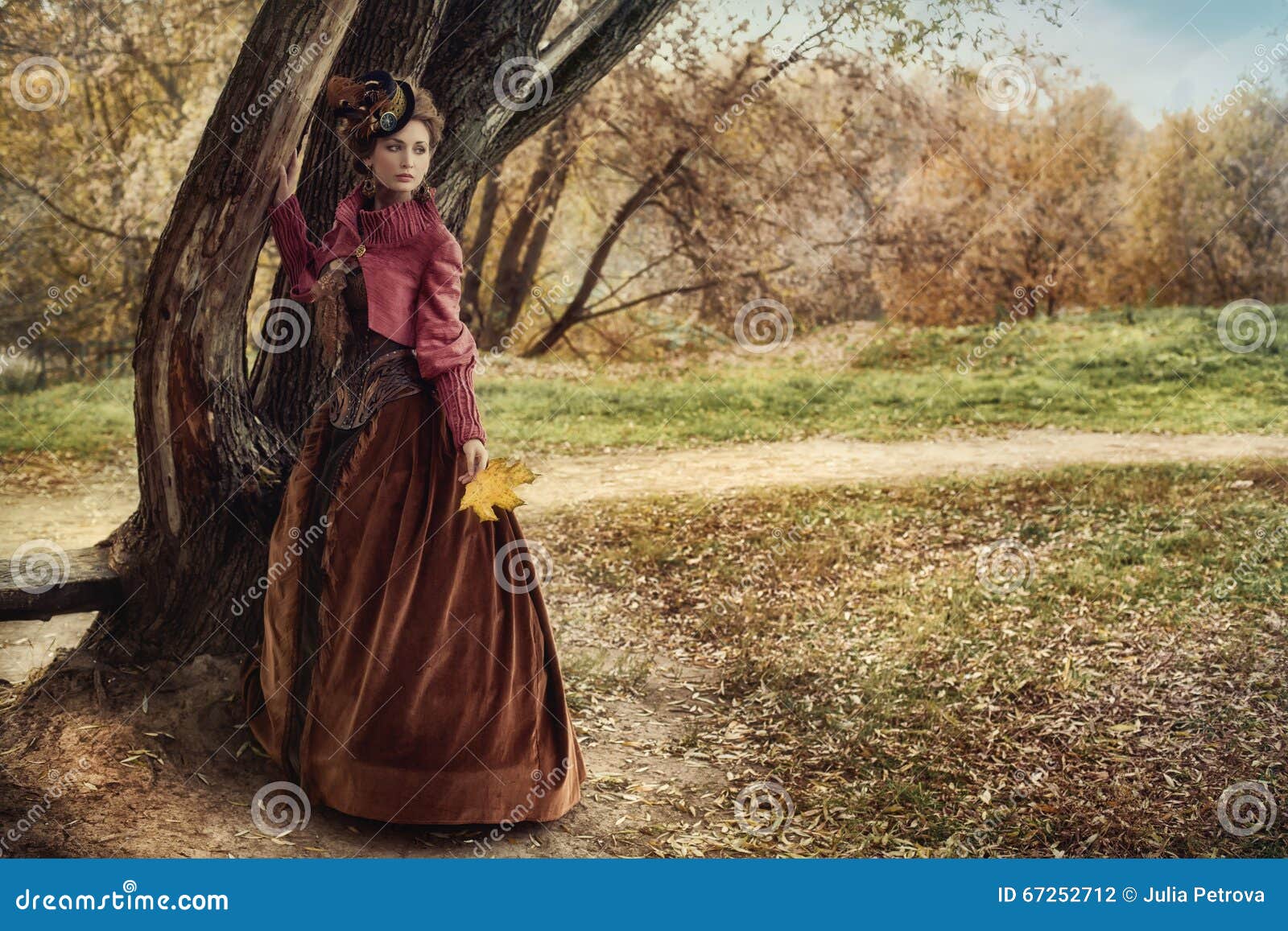 woman in historical dress near the tree in autumn forest.