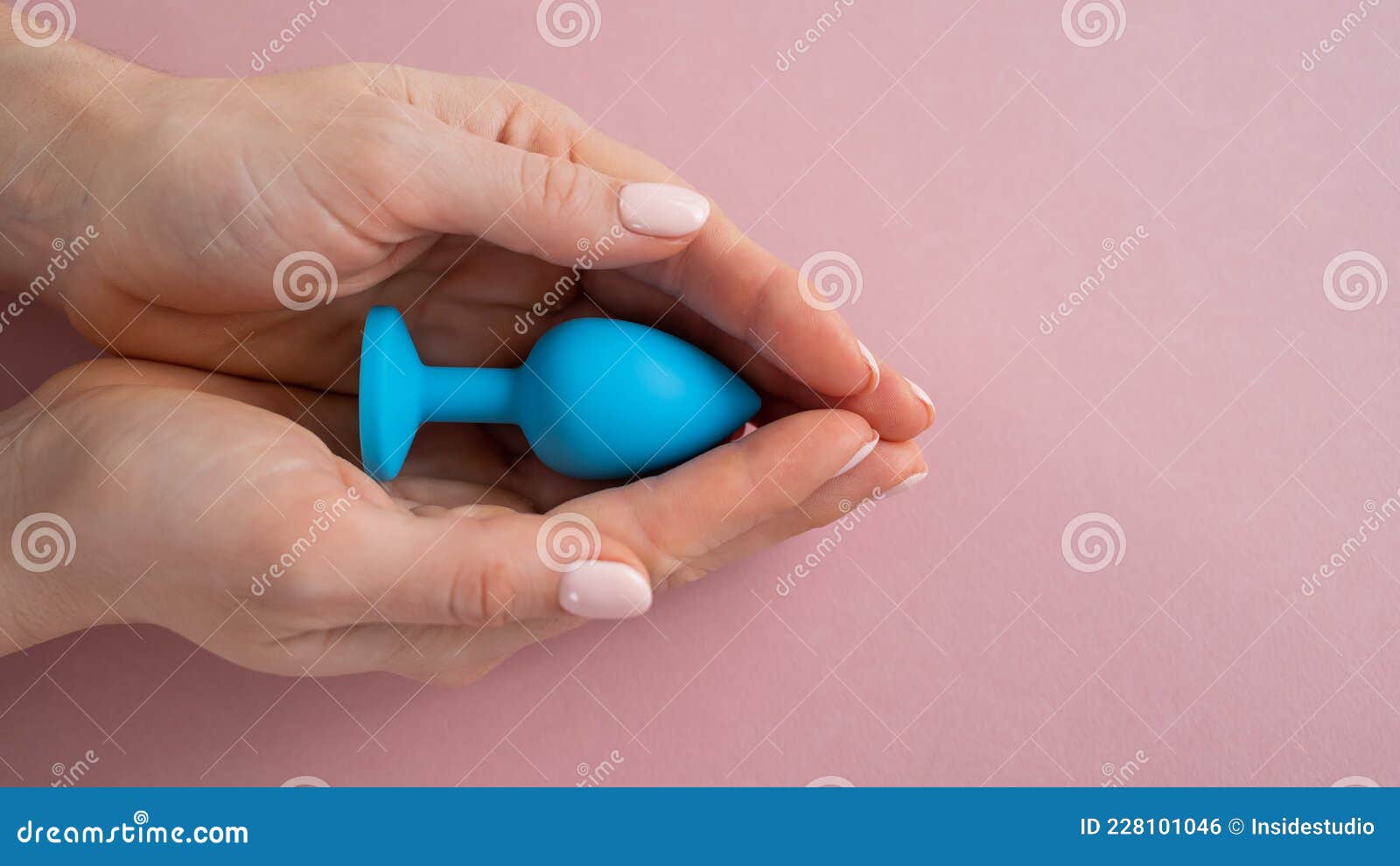 A Woman is Holding a Blue Anal Plug on a Pink Background