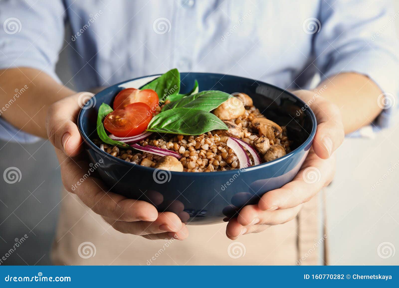 woman holding bowl of delicious buckwheat porridge with vegetables and mushrooms