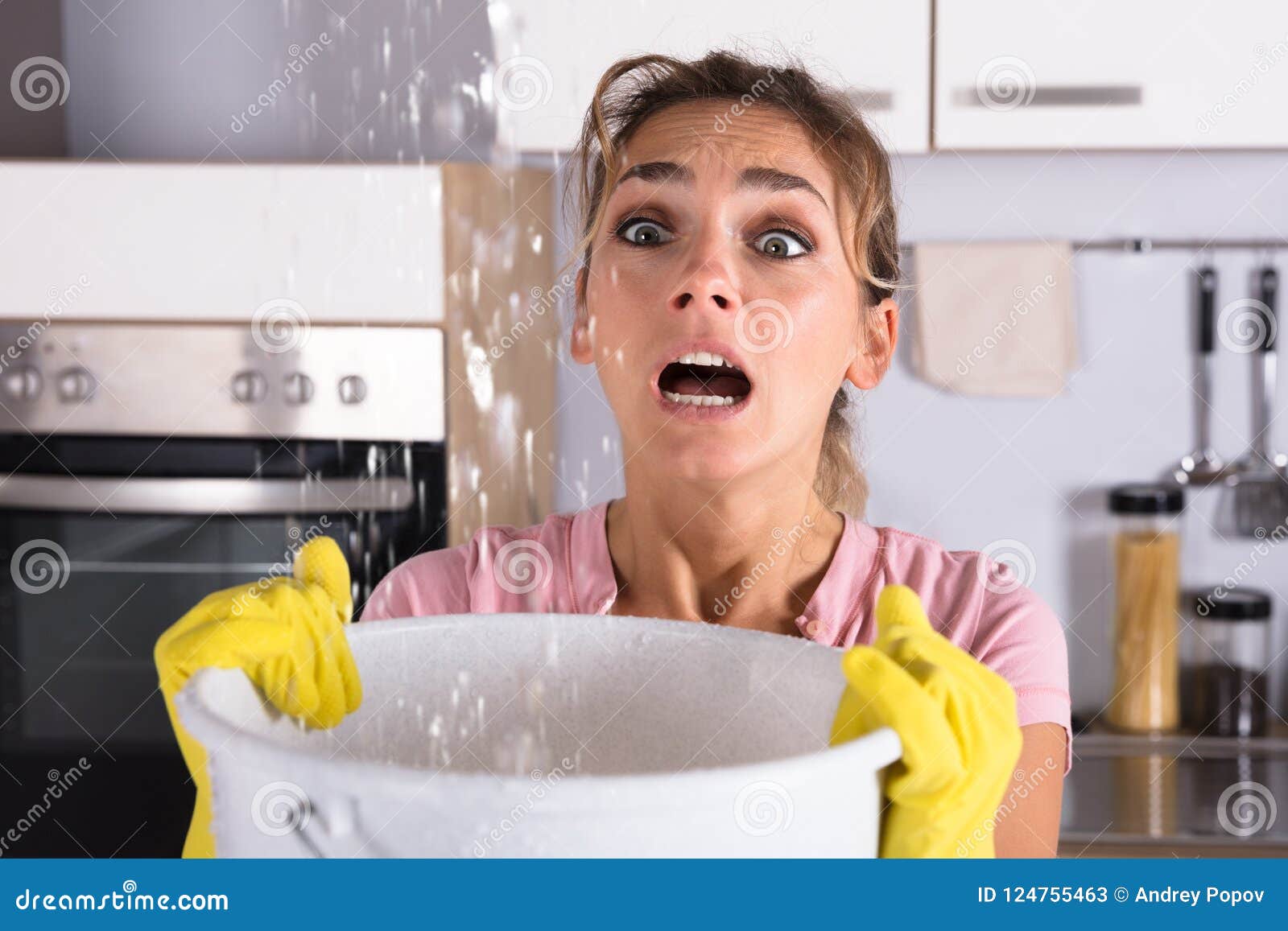 woman holding a bucket while water droplets leak from ceiling