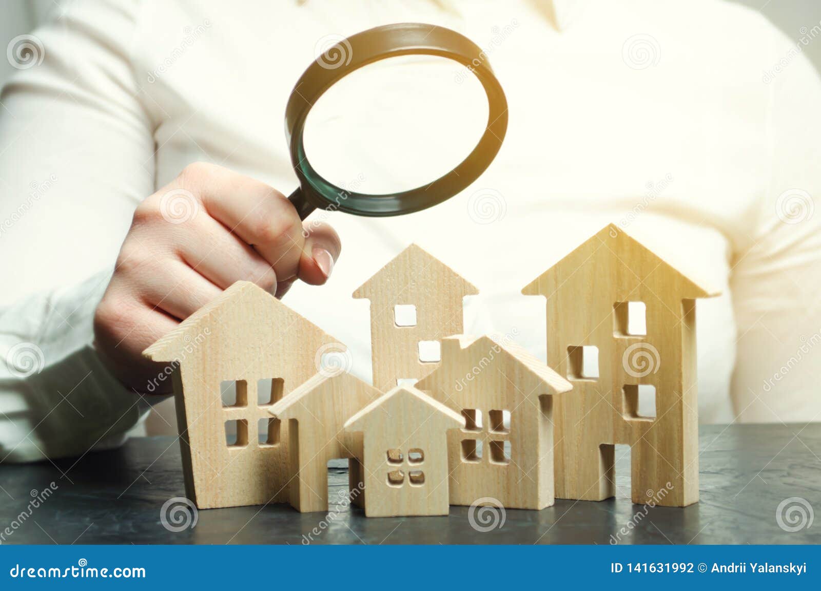 a woman is holding a magnifying glass over a wooden houses. real estate appraiser. property valuation / appraisal. find a house.