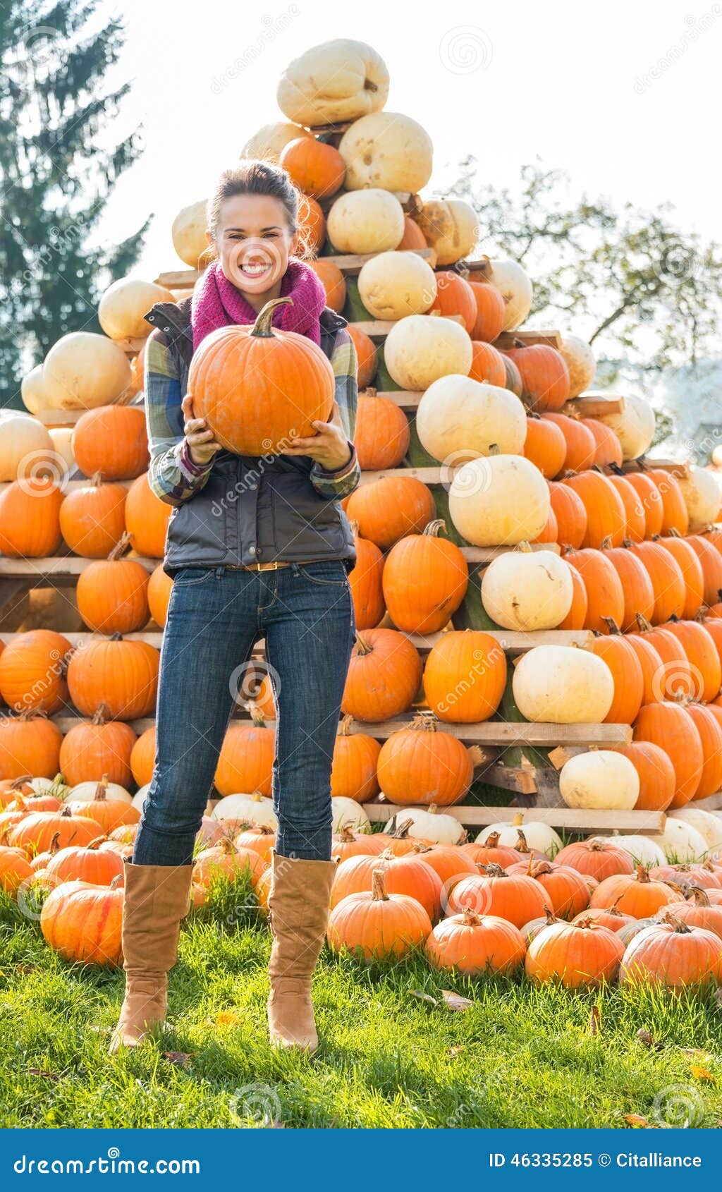 woman holding pumpkin in front of pumpkin piramide
