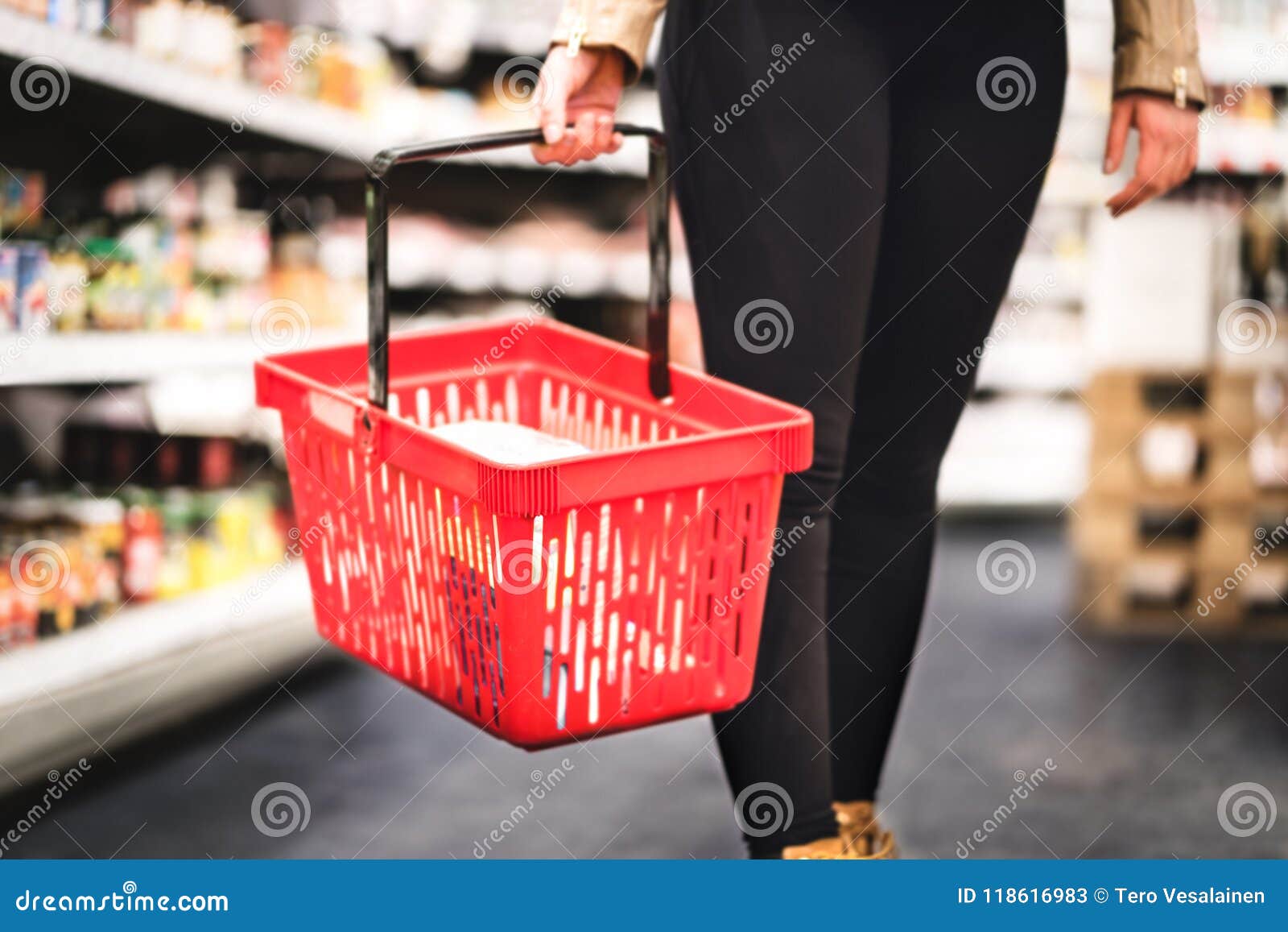 woman holding shopping basket and walking in grocery store aisle