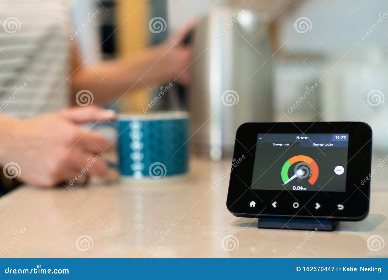 woman at home boiling kettle for hot drink with smart energy meter in foreground