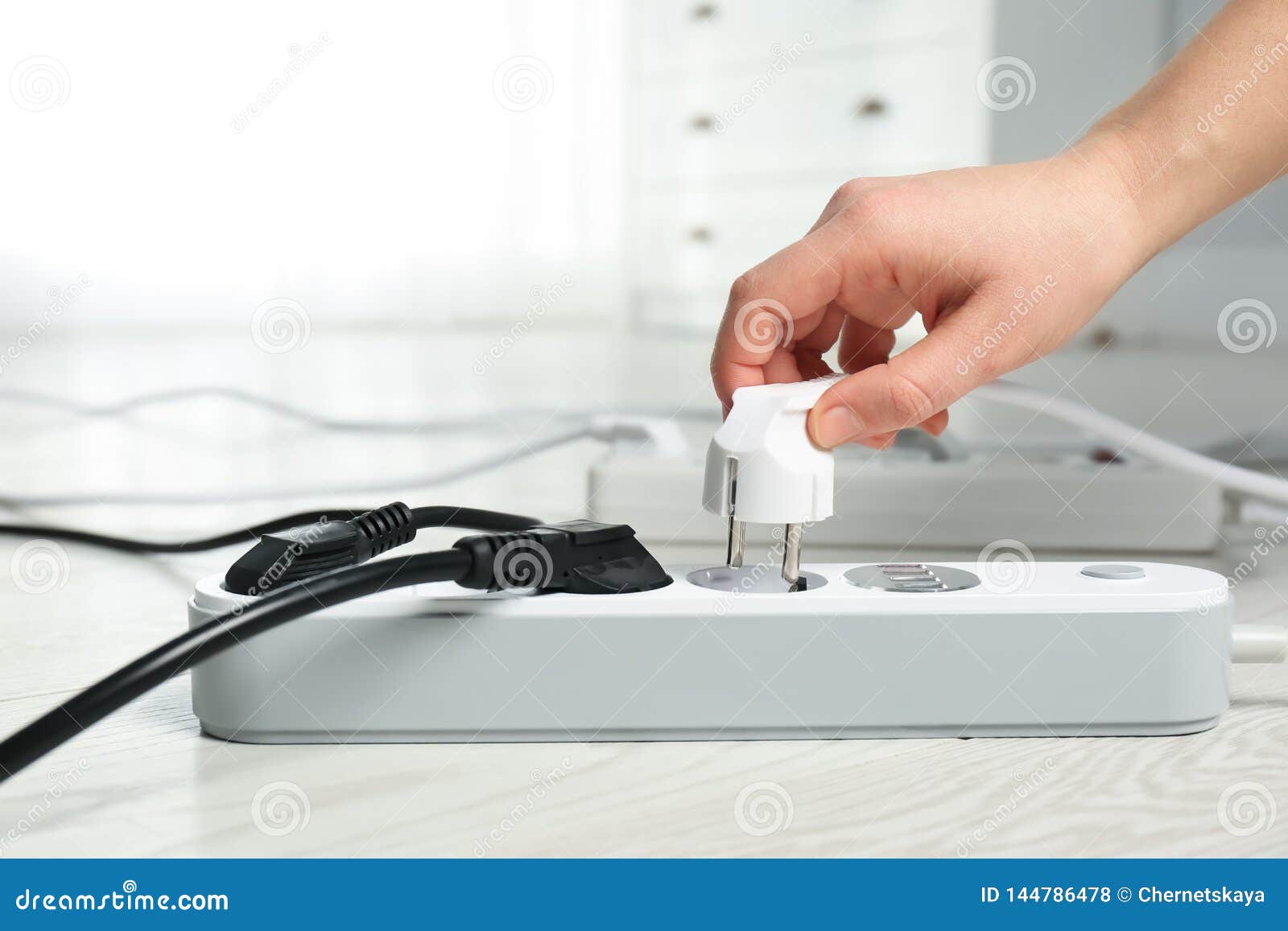 Woman Inserting Power Plug Into Extension Cord On Floor Indoors