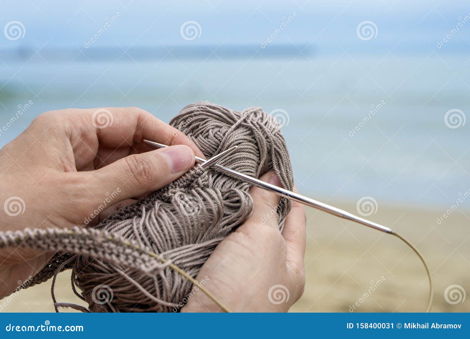 woman knits grey yarn openwork pattern with metal knittings on beach