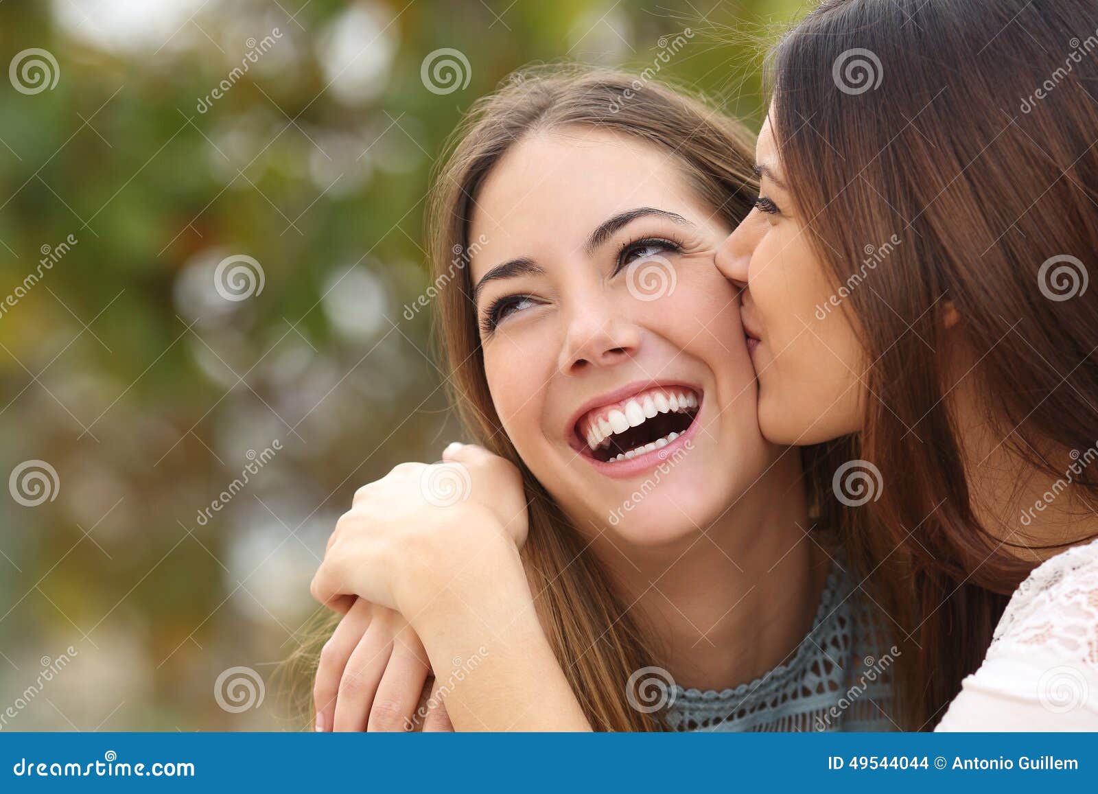 woman laughing with perfect teeth while a friend is kissing her