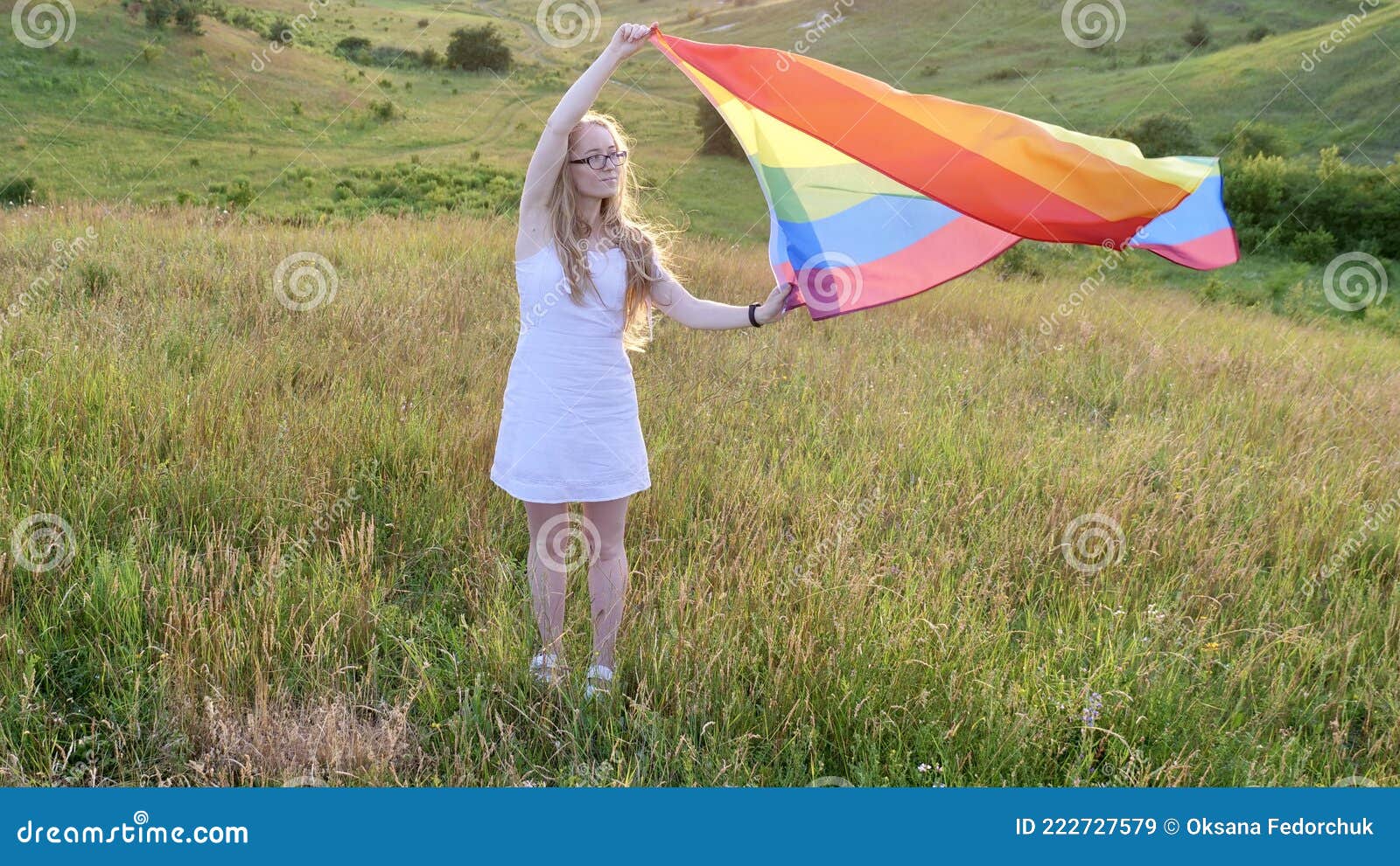 Woman lesbian with LGBT flag on a green field. Bisexual, lesbian, woman, person, homosexual holds LGBT flag on the green hills on a sunny day sunset and celebrating a gay parade, Bisexuality Day or National Coming Out Day in pride month