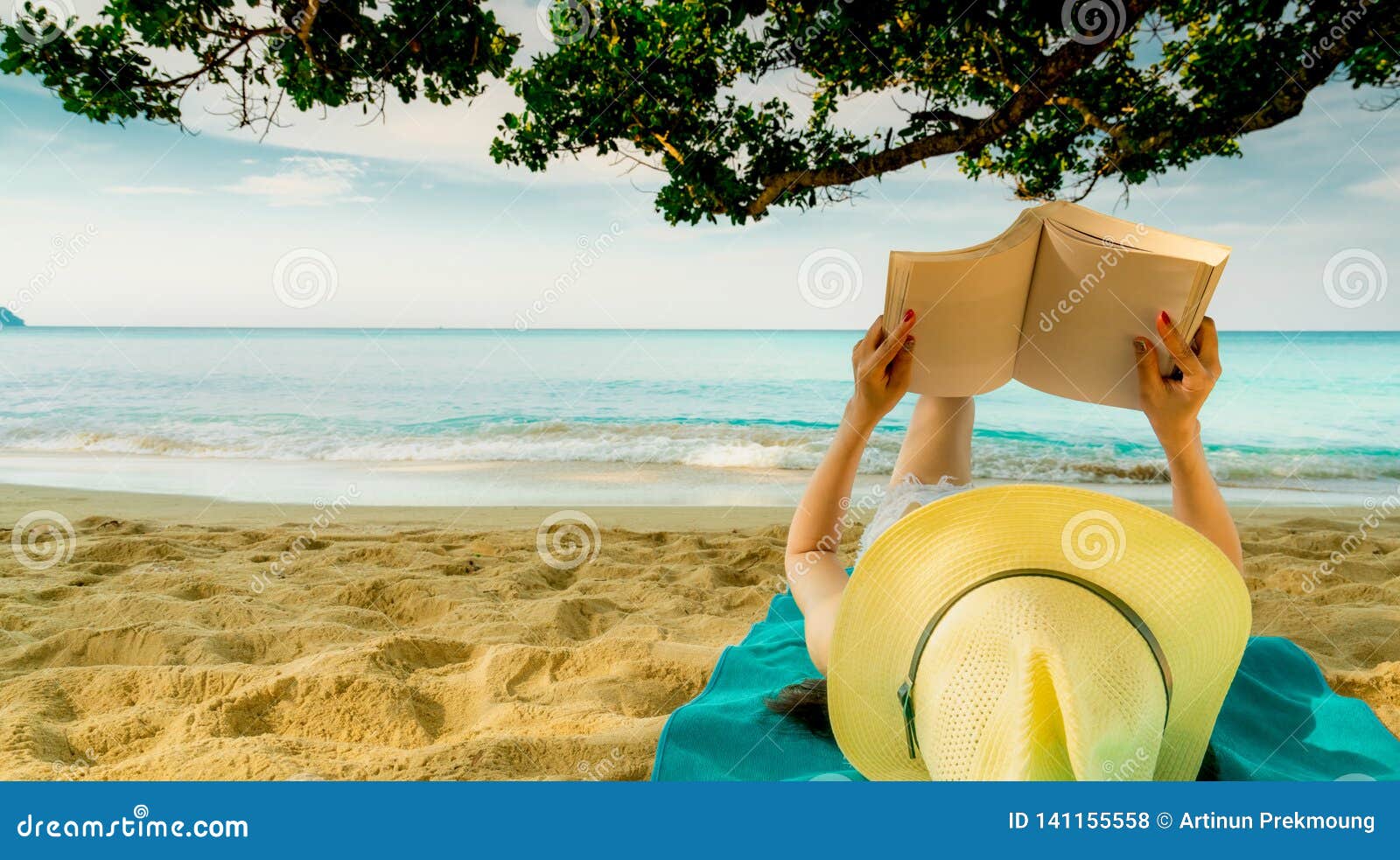 woman lie down on green towel that put on sand beach under the tree and reading a book. slow life on summer vacation. asian woman