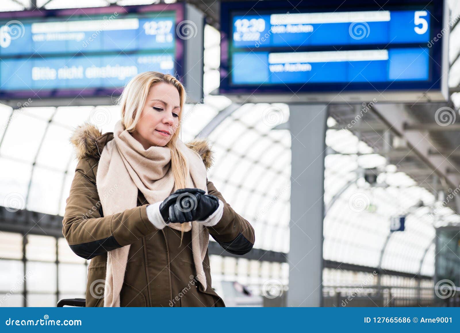 woman looking at wristwatch in train station as her train has a delay