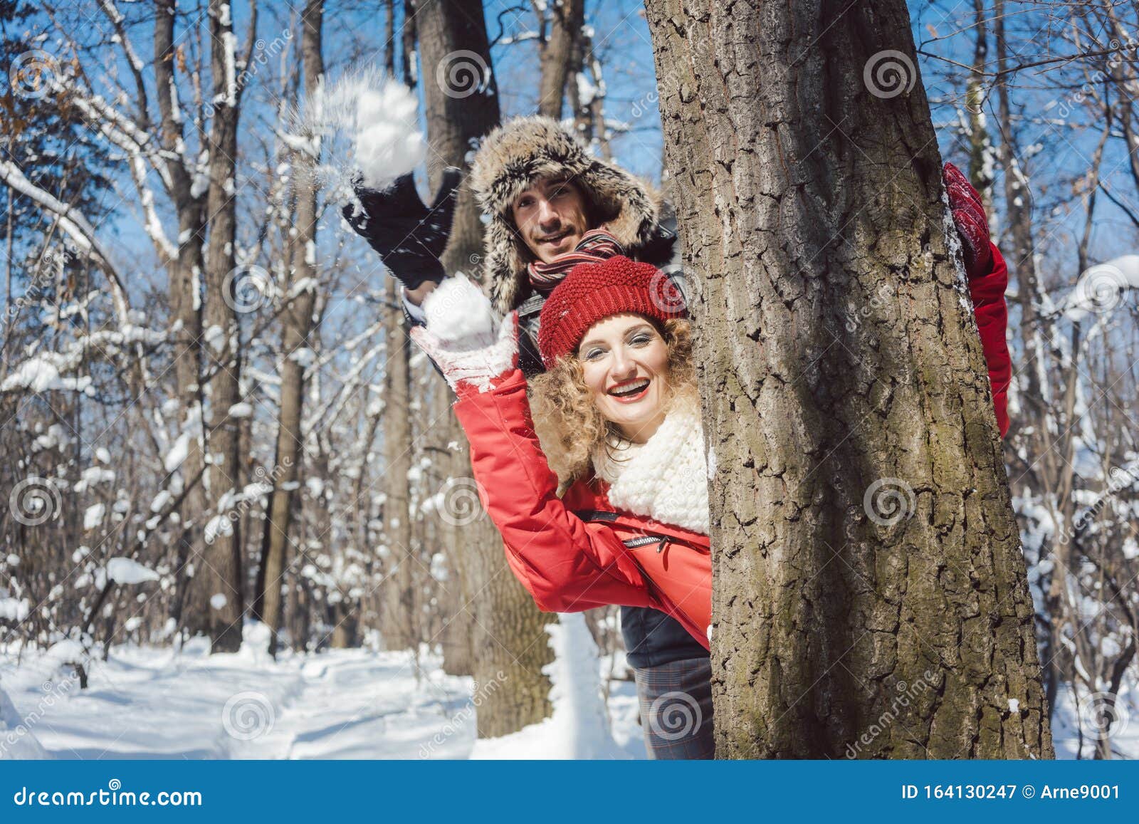 Woman and Man in Winter Throwing Snowball Hiding Behind a Tree Stock