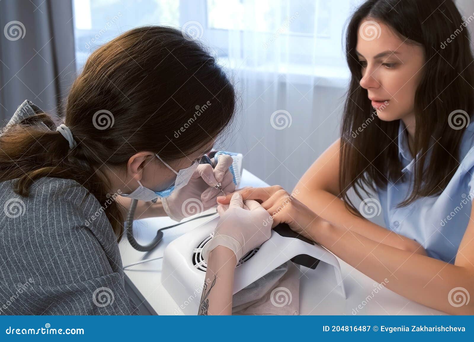 woman manicurist in mask cleaning pterygium on client`s nail using apparatus.