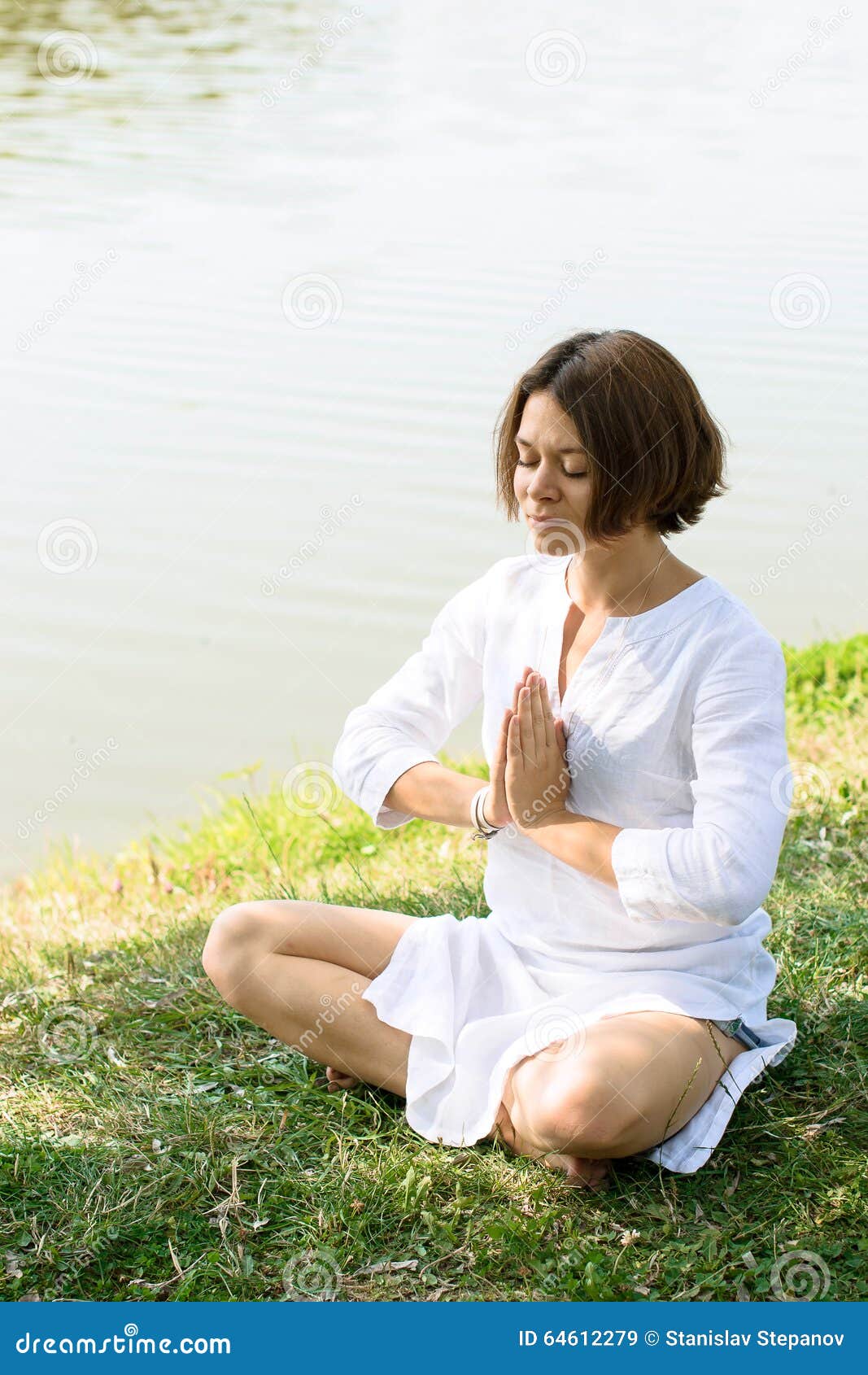 woman meditating in easy pose on the grass at the river-bank.