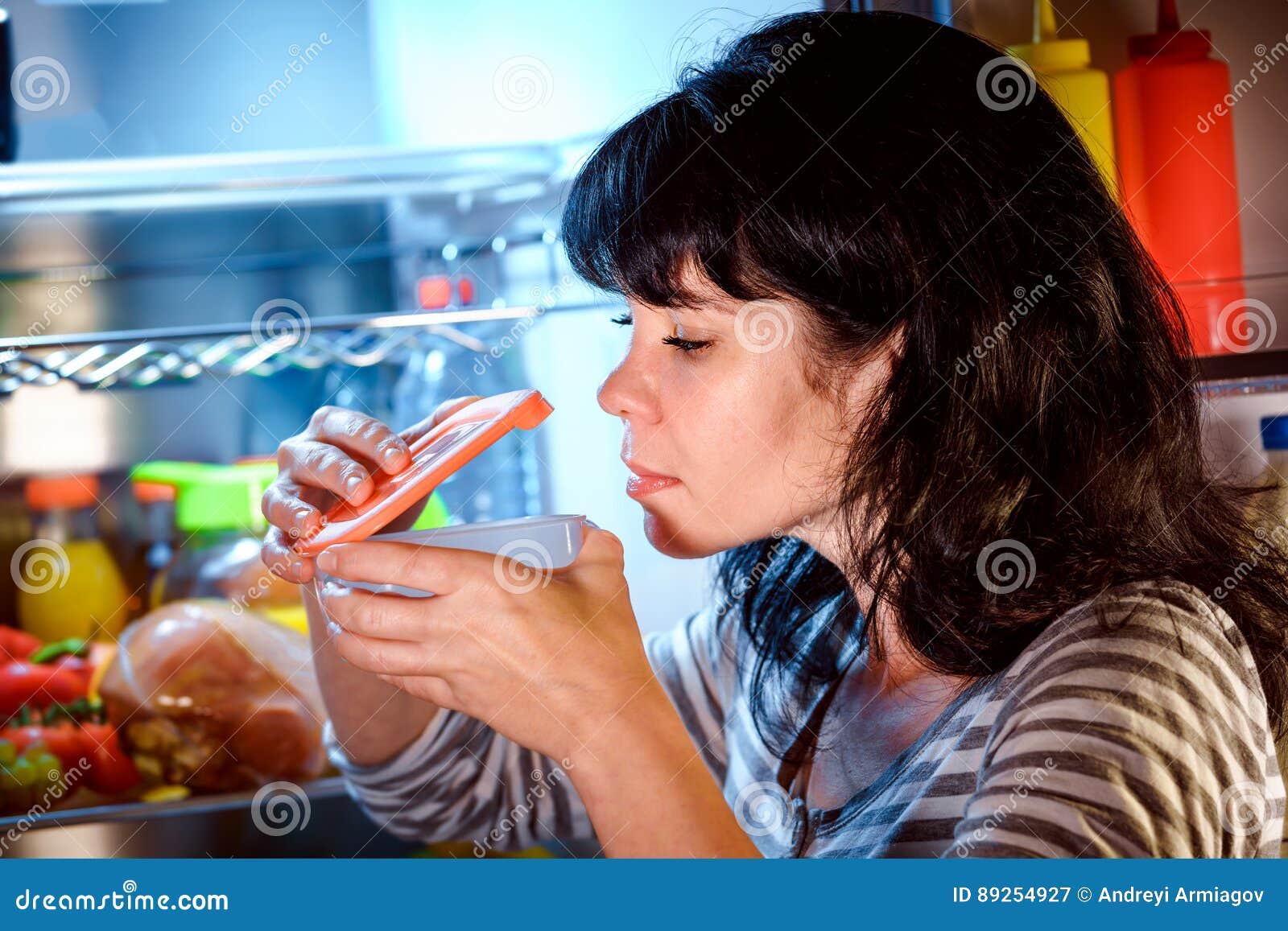 woman opened the refrigerator and sniffs a container of food
