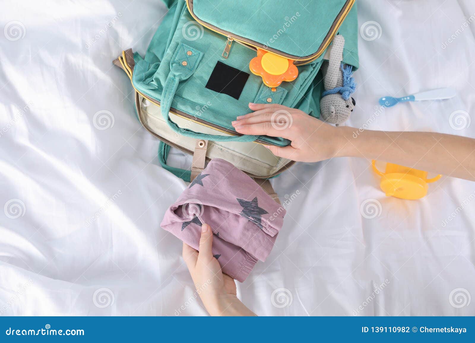 woman packing baby accessories into maternity backpack on bed