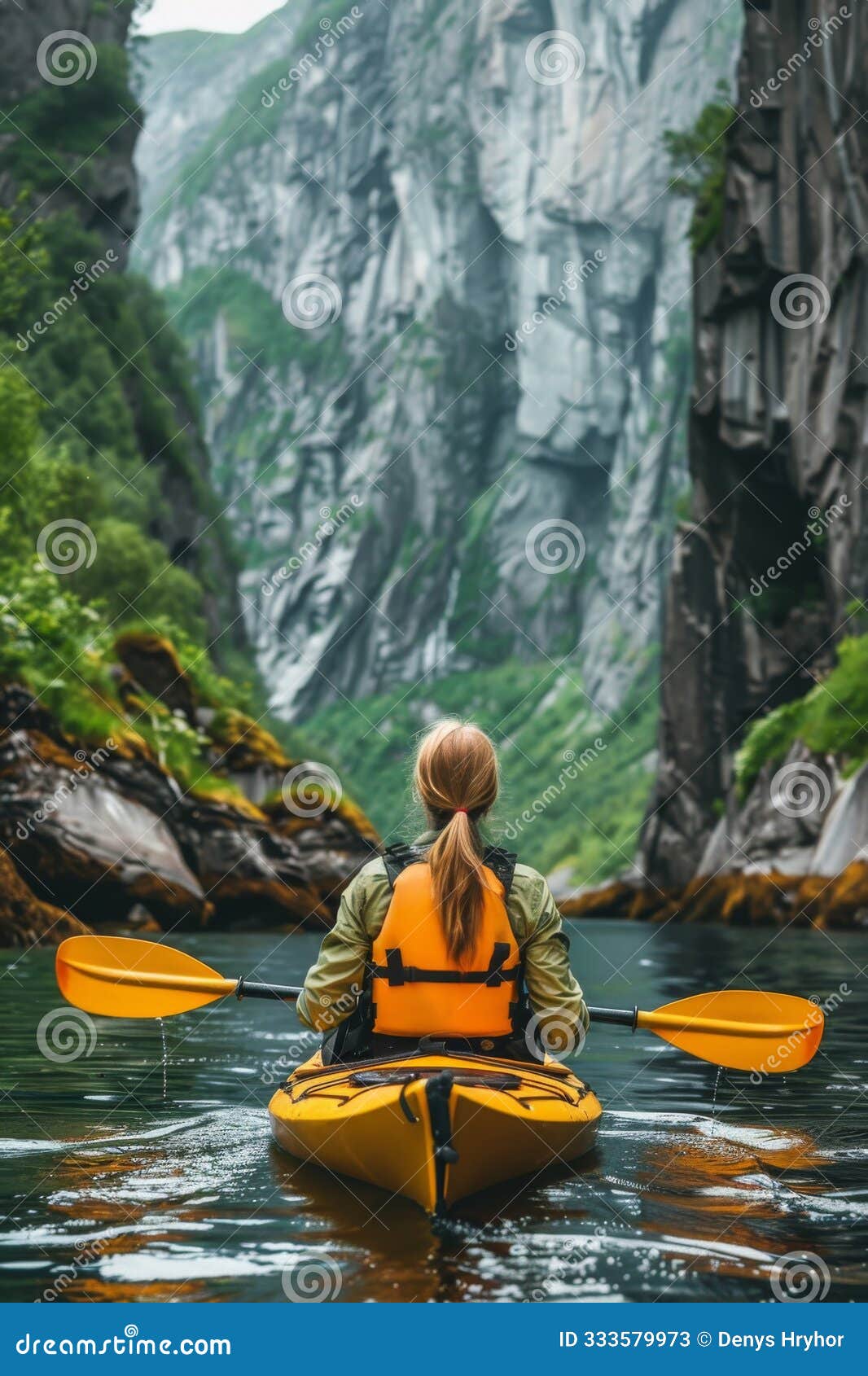 a woman paddles a kayak through the breathtaking fjords of norway, surrounded by towering cliffs and lush greenery