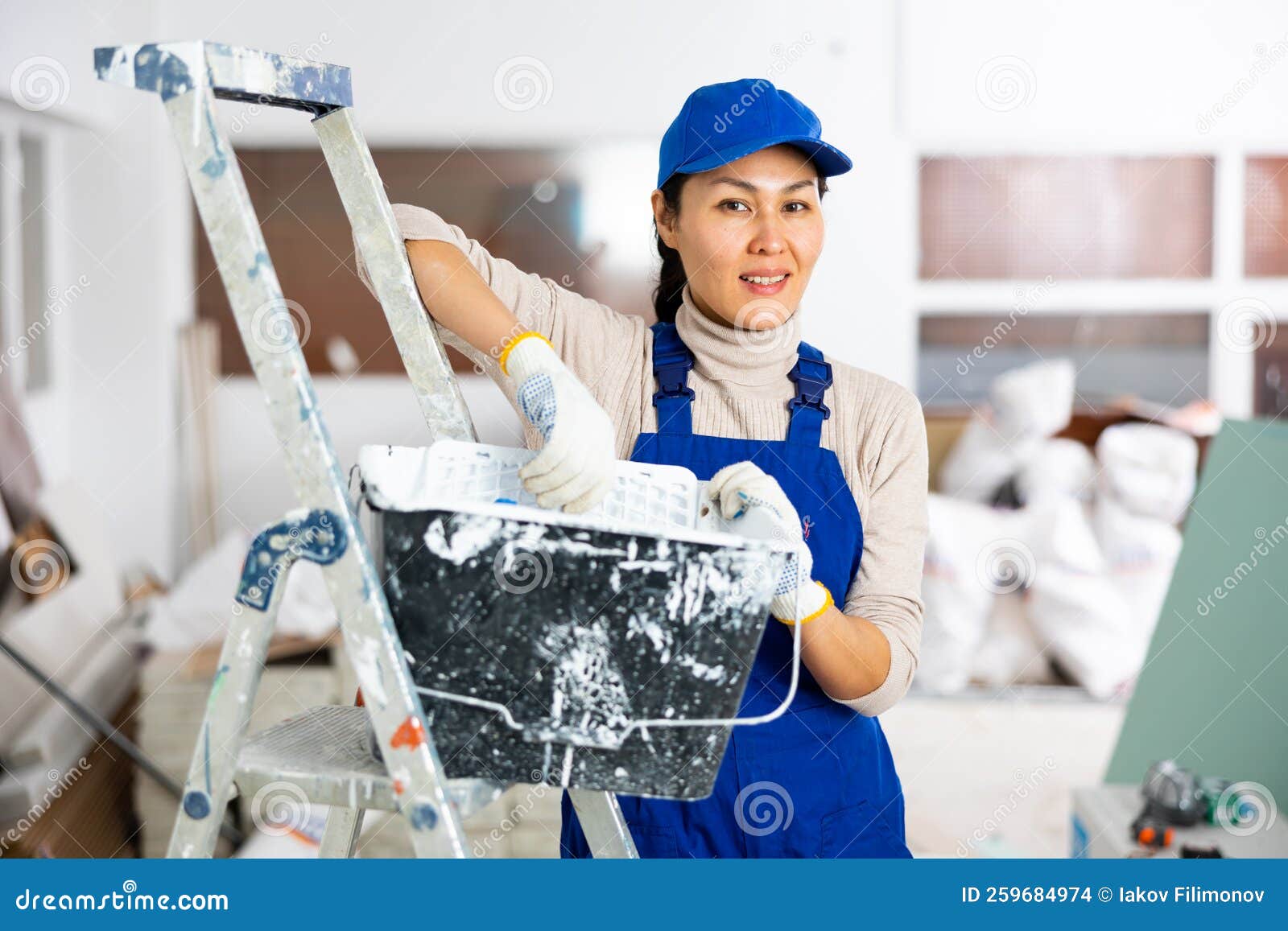Woman Painter in Overalls with Paint Roller in Building Under
