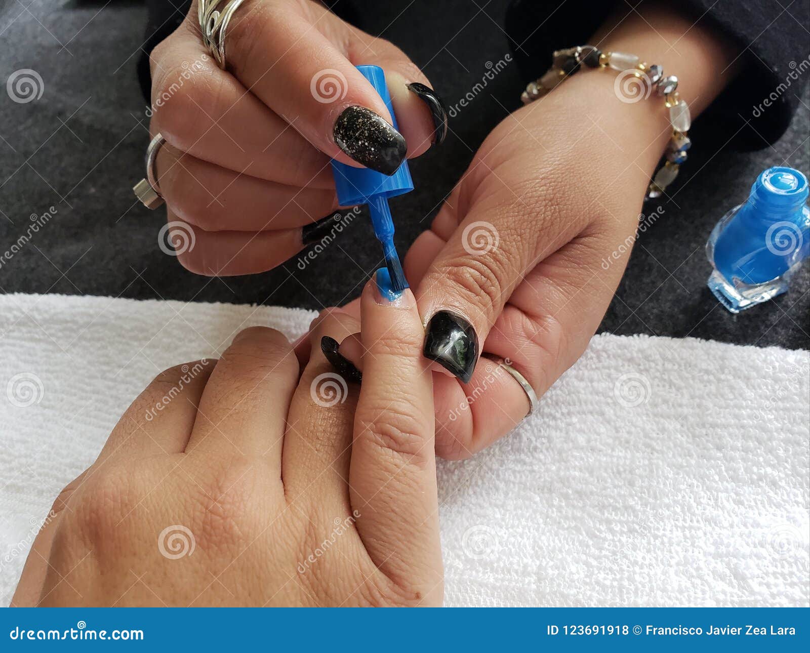 woman painting the fingernails of another woman with blue nail polish