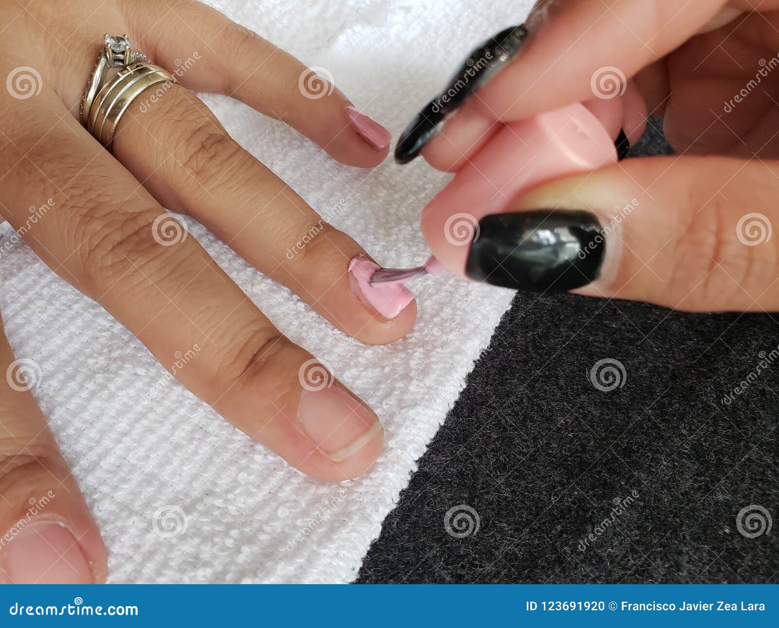 woman painting the fingernails of another woman with light pink nail polish