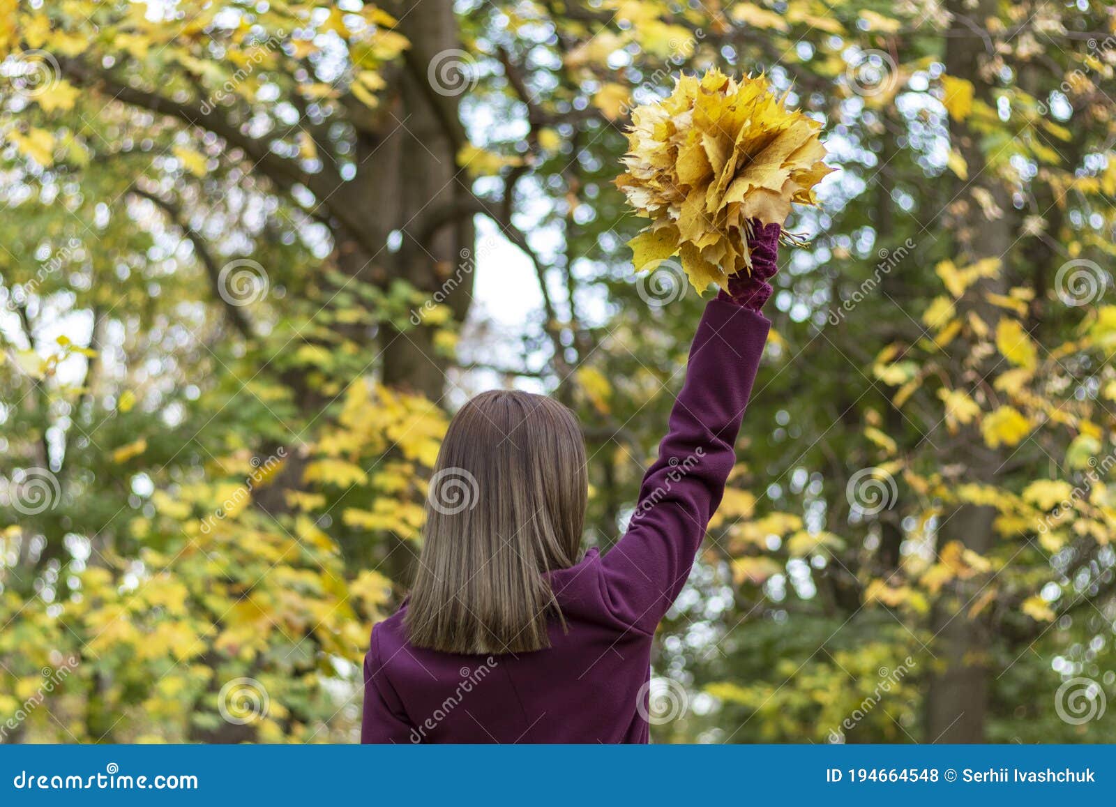 woman in park holds autumn leaf bouquet. view from back