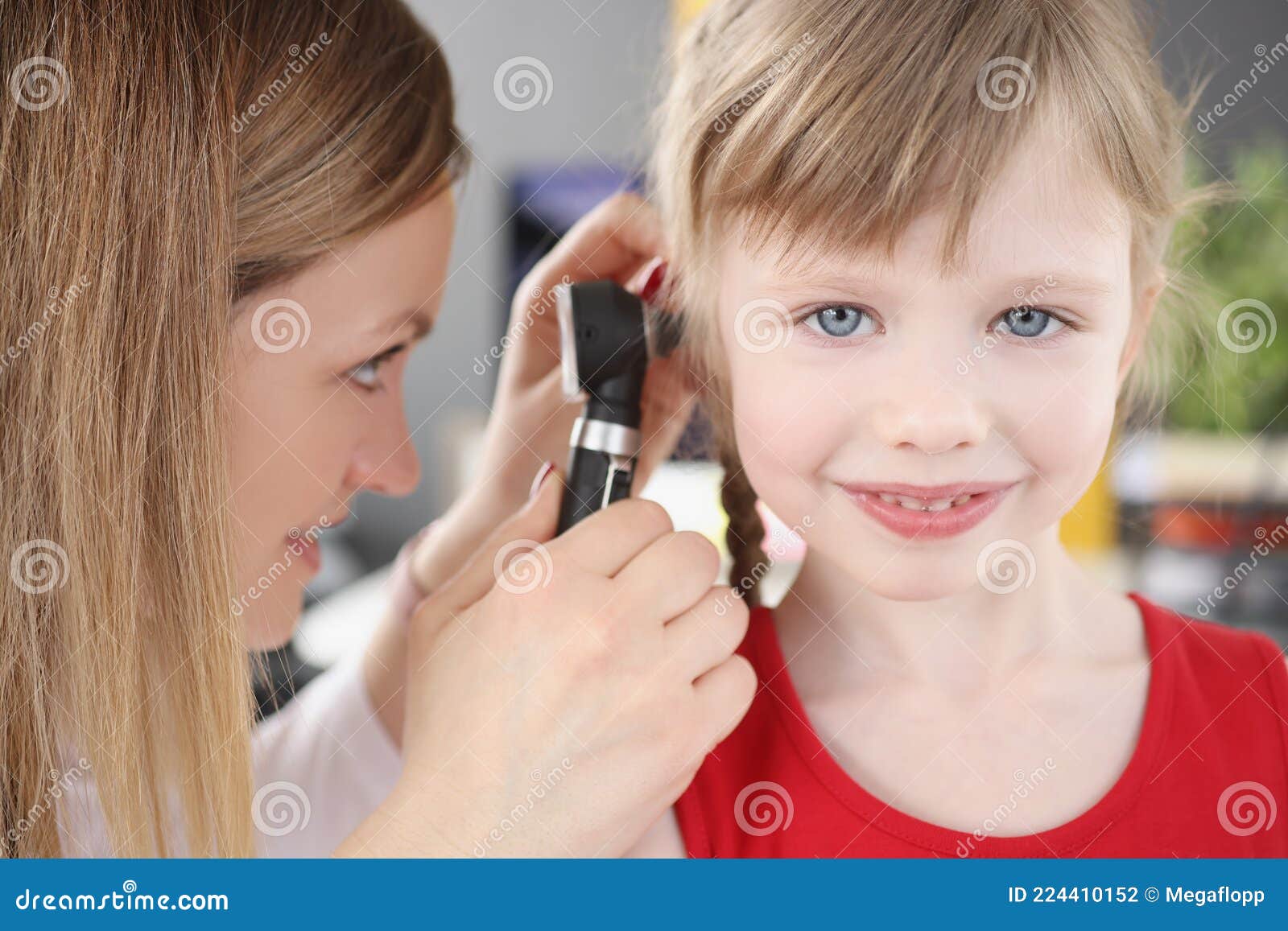 woman pediatrician looking at eardrum of little girl using otoscope in clinic