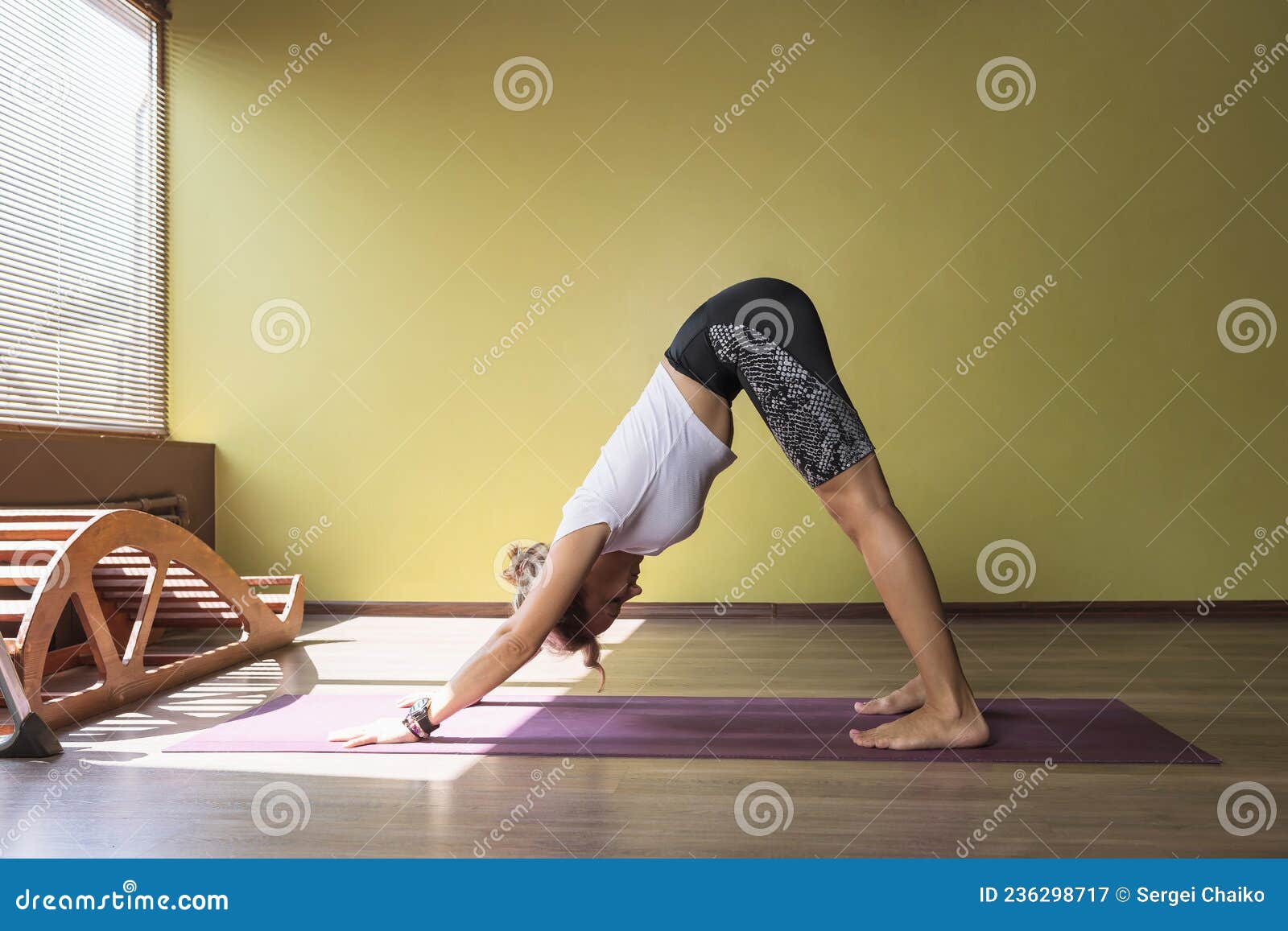 a woman performs the exercise adho mukha svanasana, dog face down pose, exercising in sportswear on a mat in the studio