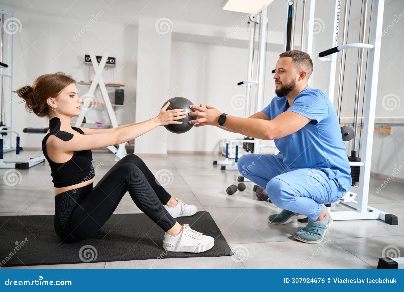 woman performs exercises with a ball under supervision of kinesiologist