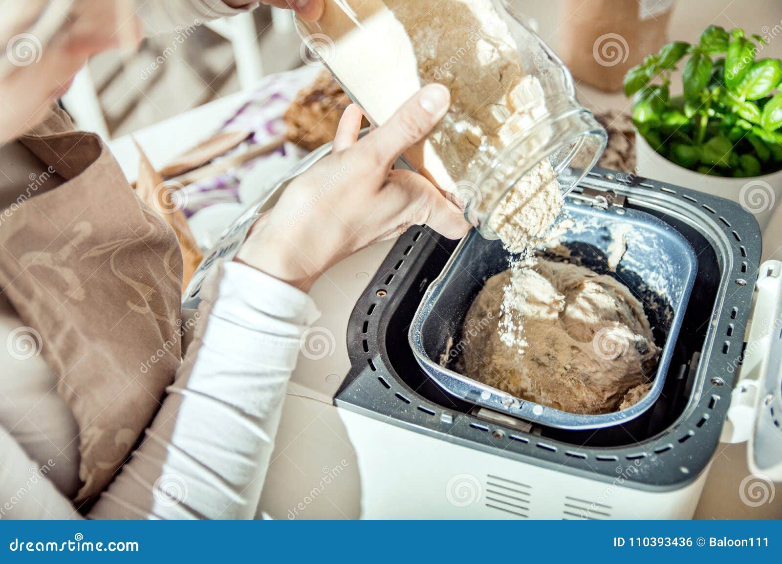 woman pours ingredients into the bread maker machine