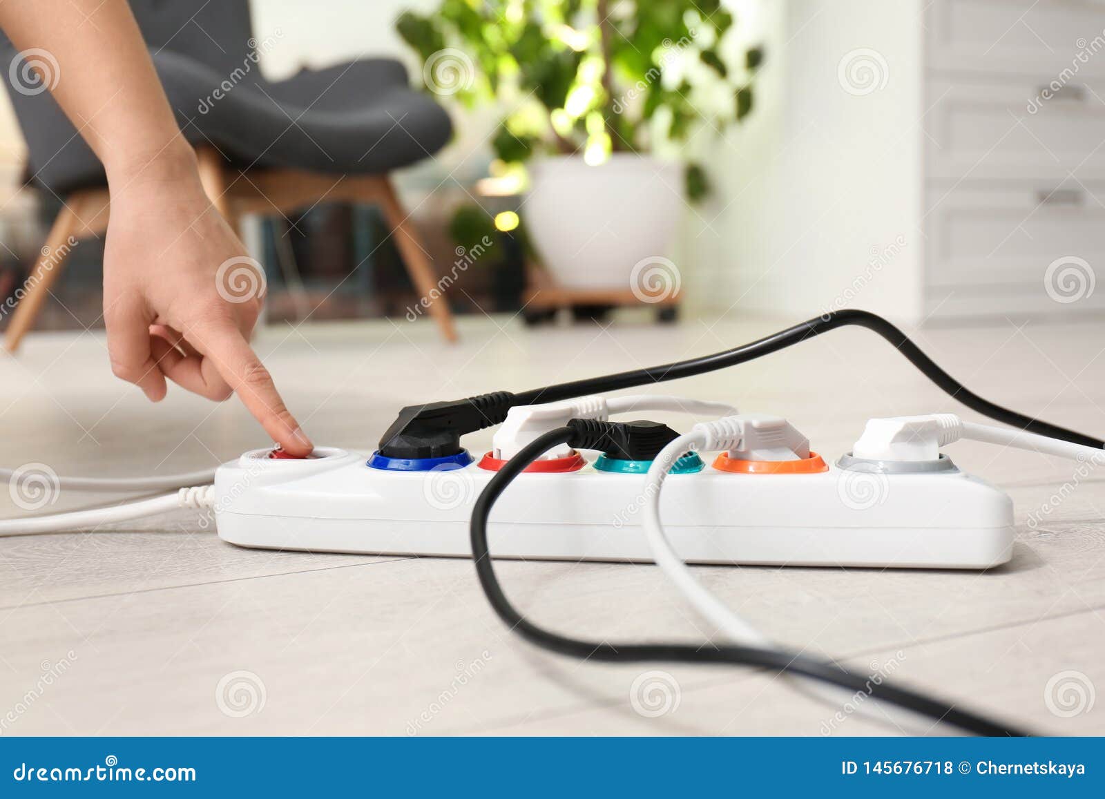 Woman Pressing Power Button Of Extension Cord On Floor Indoors