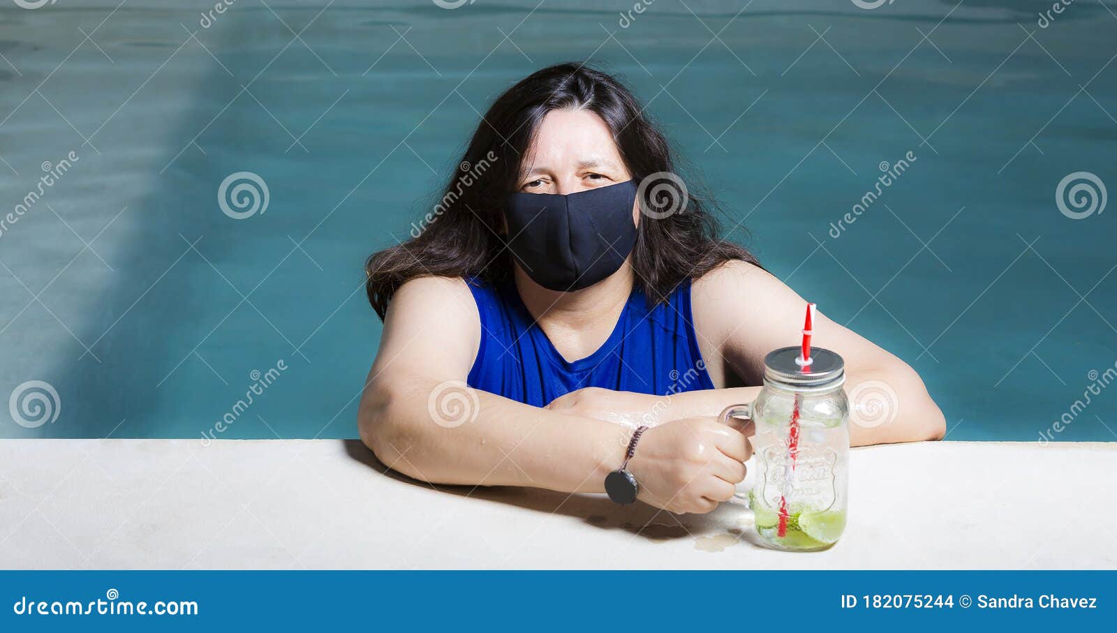 woman with protective mask inside pool and enjoying a cold drink. these measures of social isolation and protection are due to the