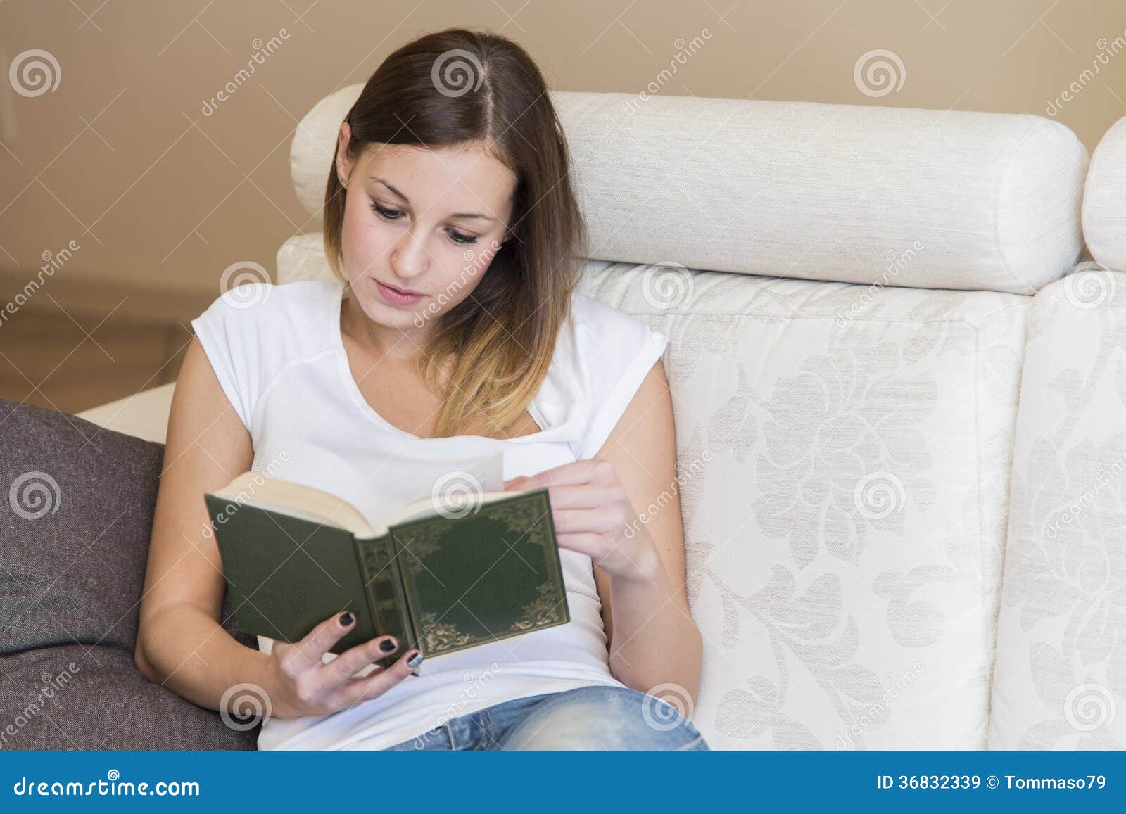 Woman reading book home. Happy young woman reading a book on the sofa at home