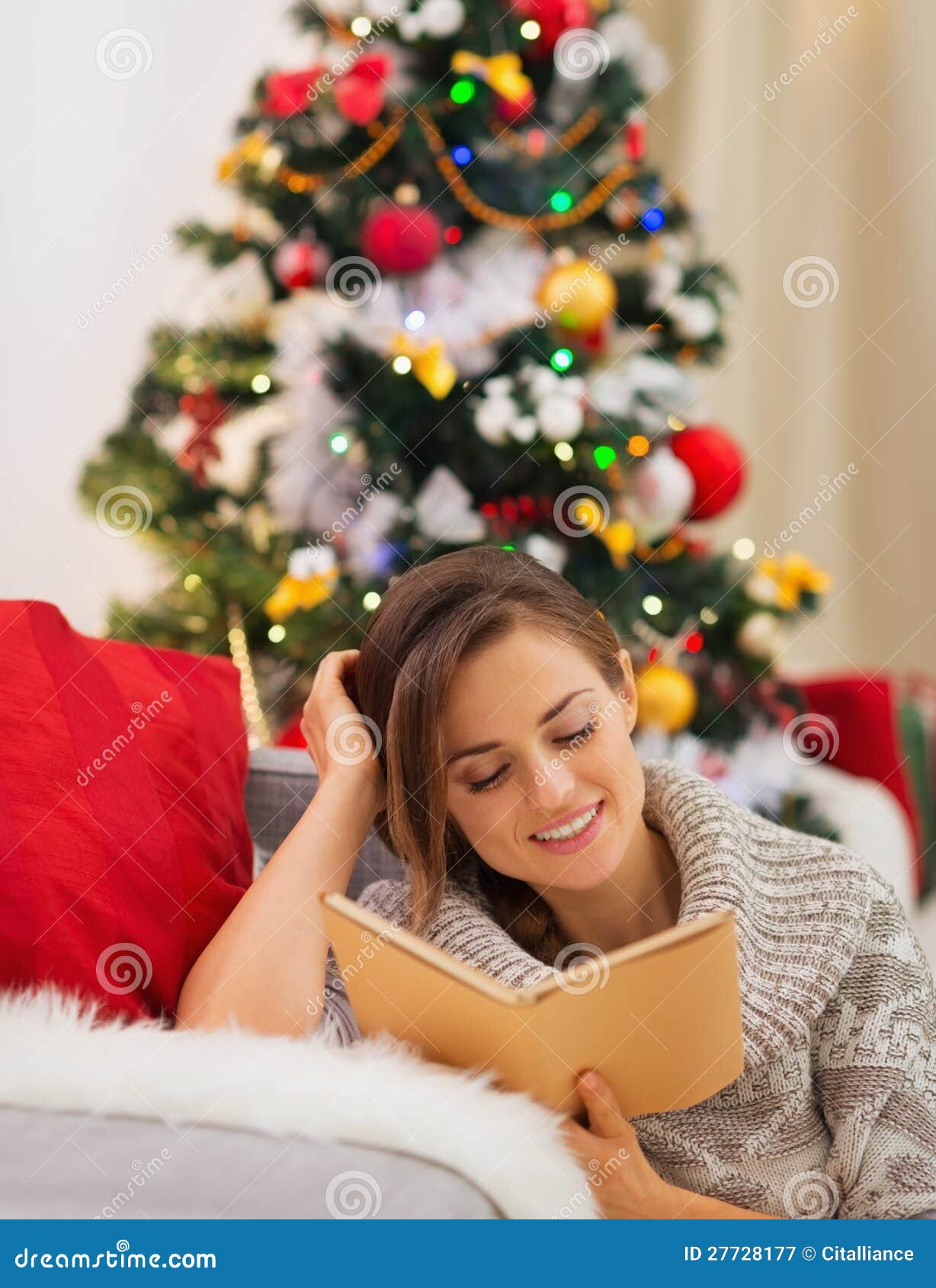 Young woman reading book near Christmas tree