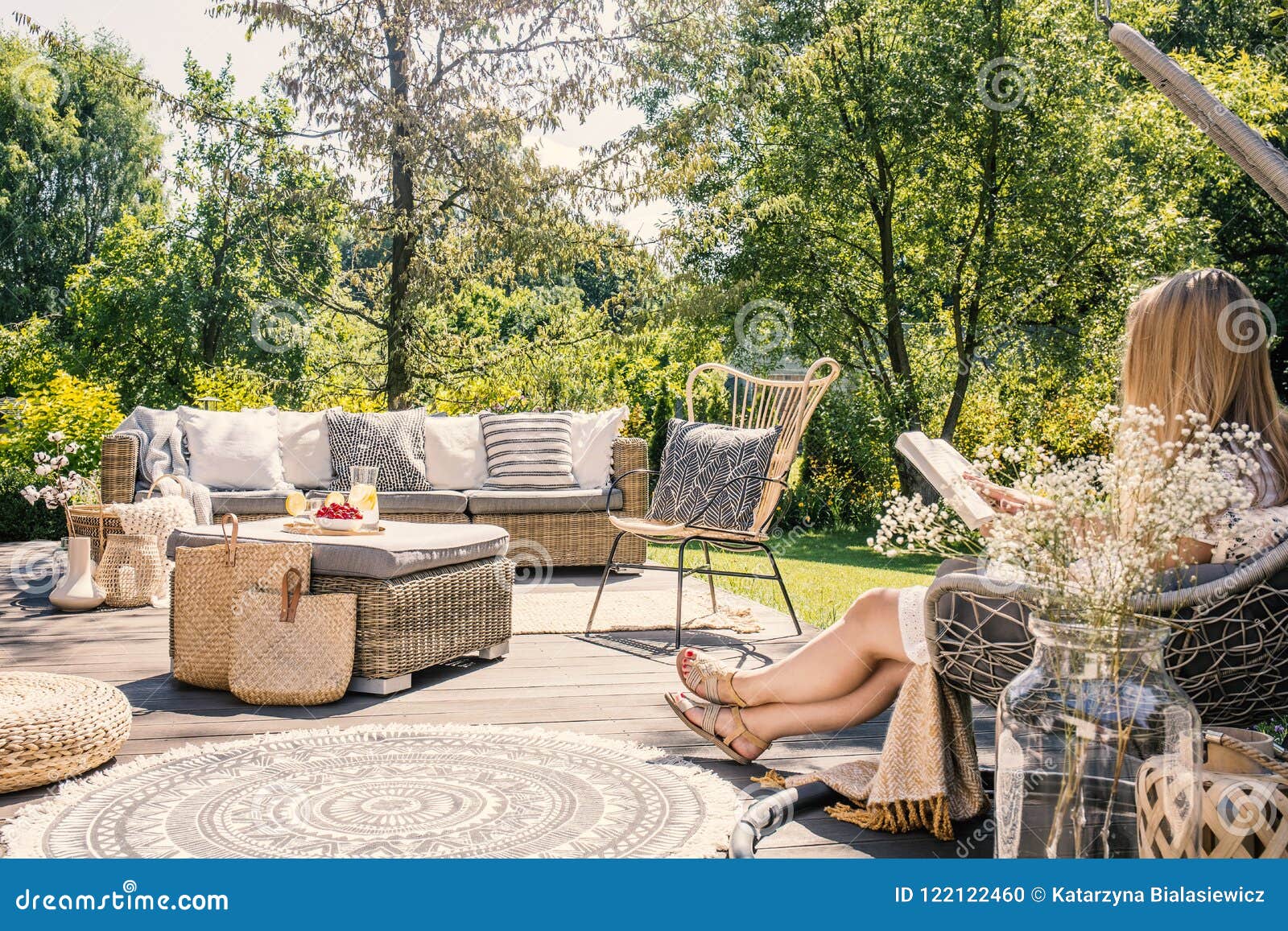 woman reading book while relaxing at terrace with rattan furniture in the garden. real photo