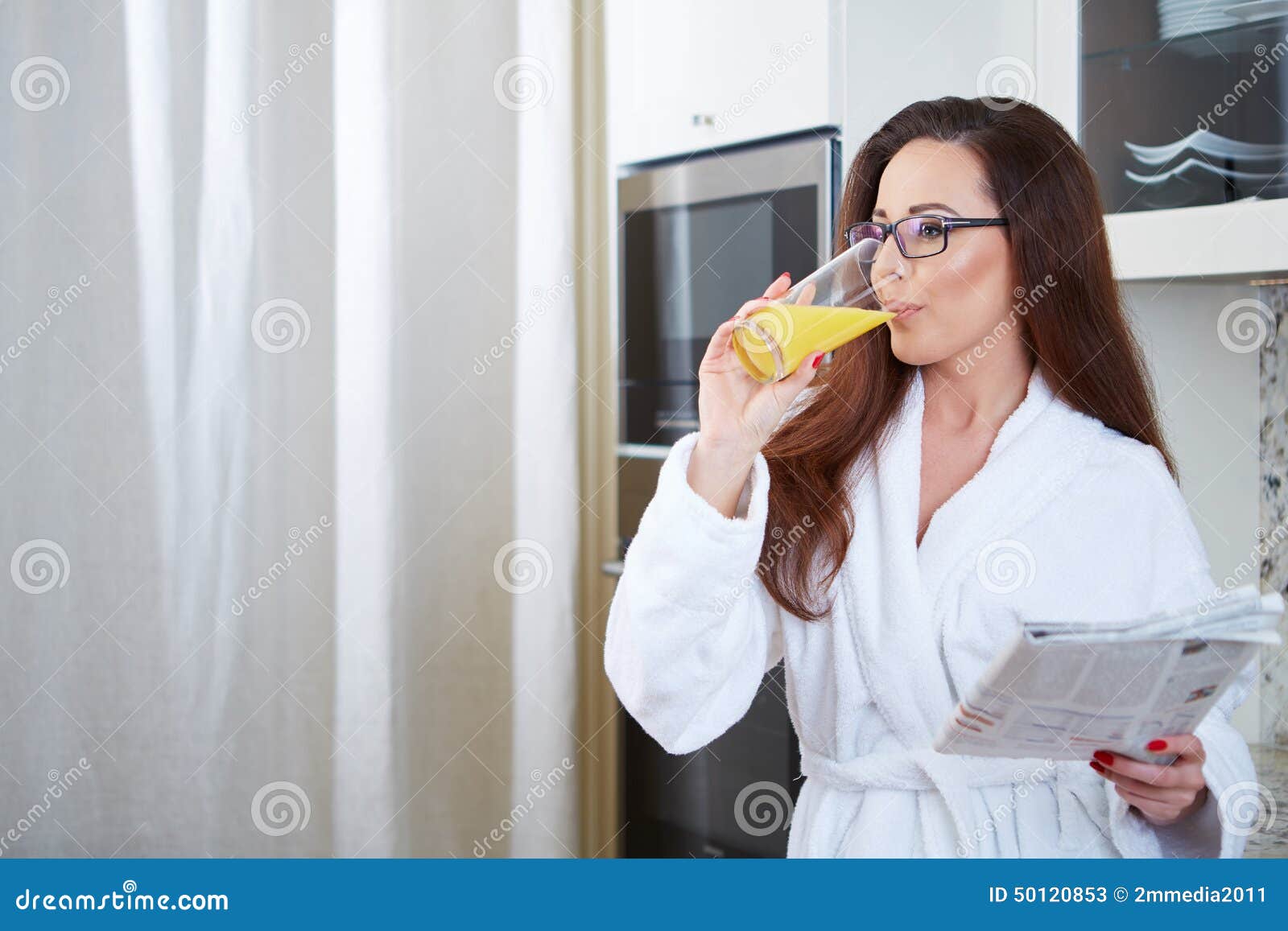 Woman reading the news while drinking orange juice in her kitchen