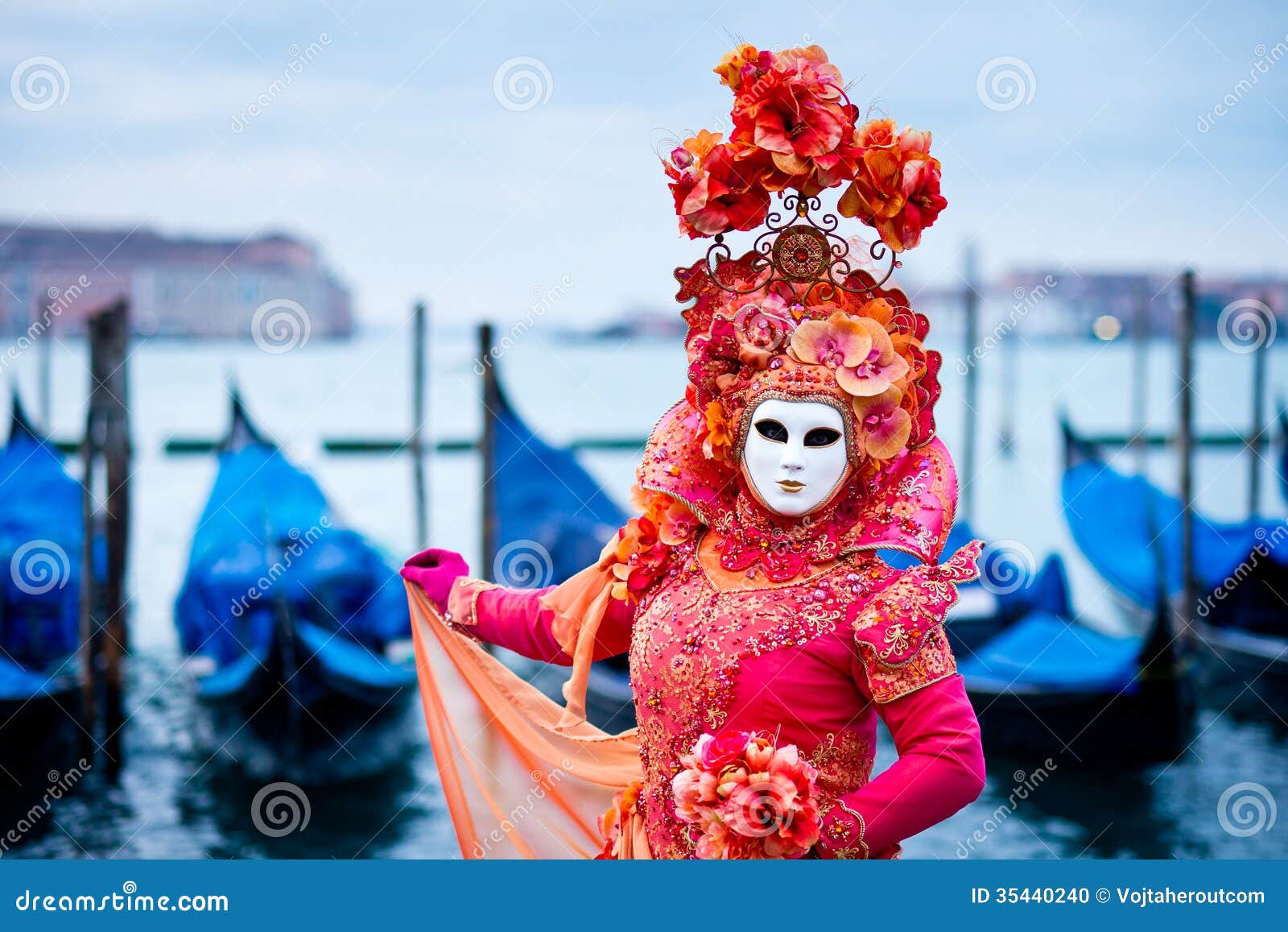 woman in red dress masked for venice carnival in front of typical gondola boats