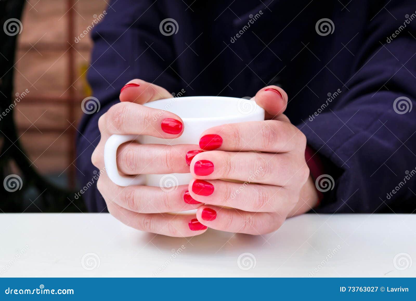 woman with red nail polish holding white cup in a cafee