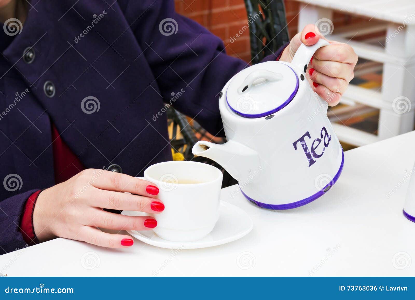 woman with red nail polish pouring a tee in a cup in a cafee