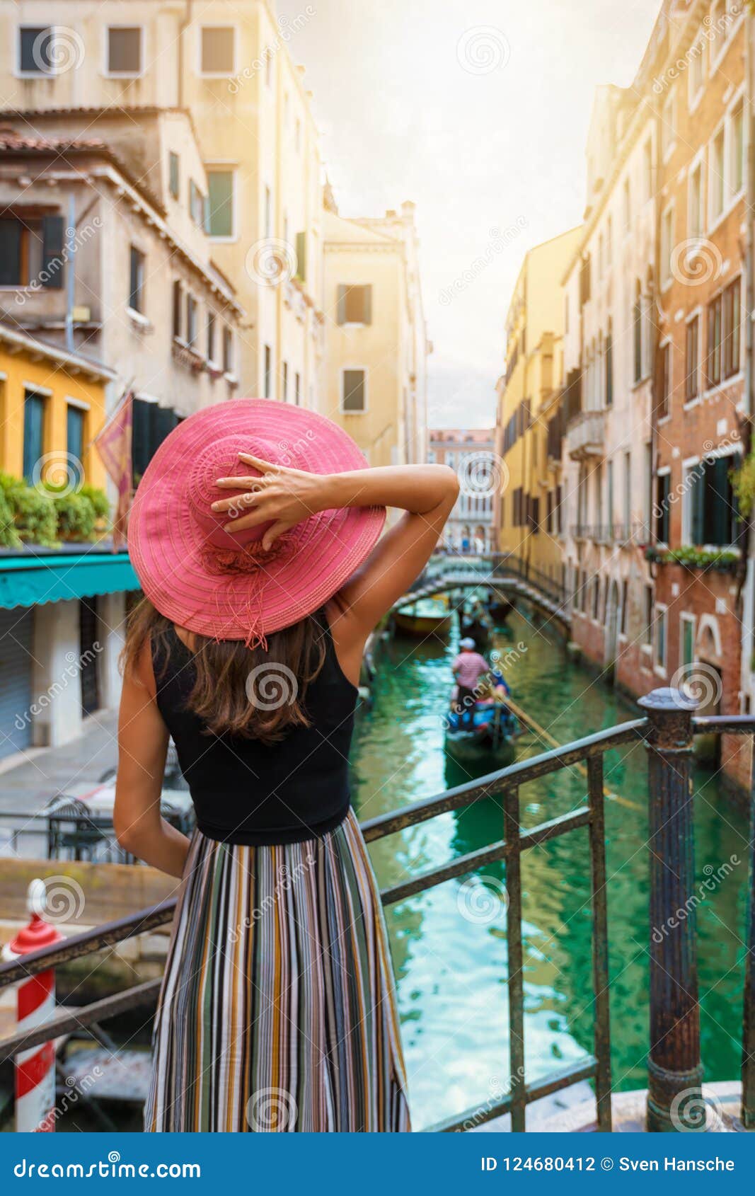 woman with red sunhat enjoys the view to a canal in venice, italy