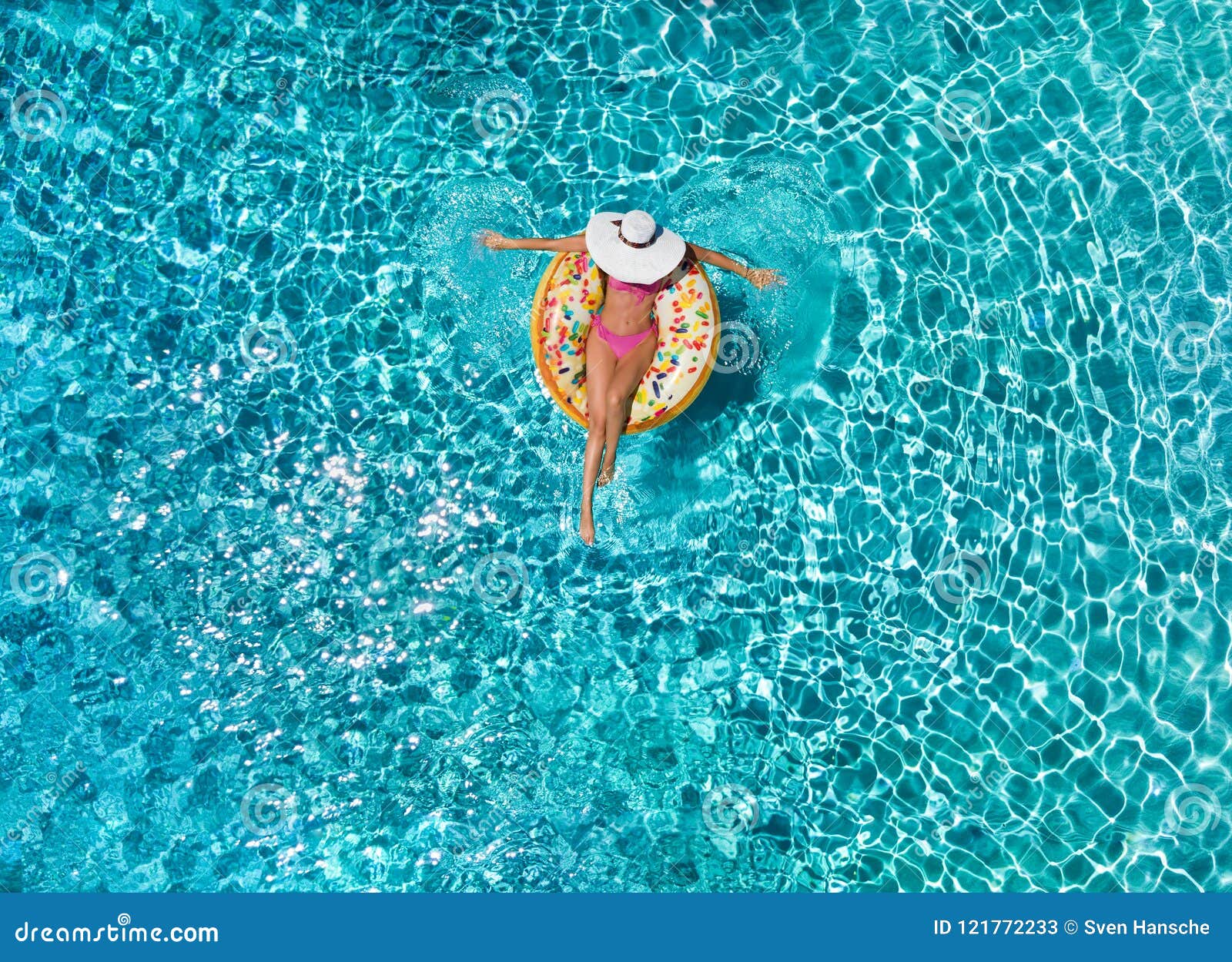 woman relaxes on a donut d float over blue, sparkling pool water
