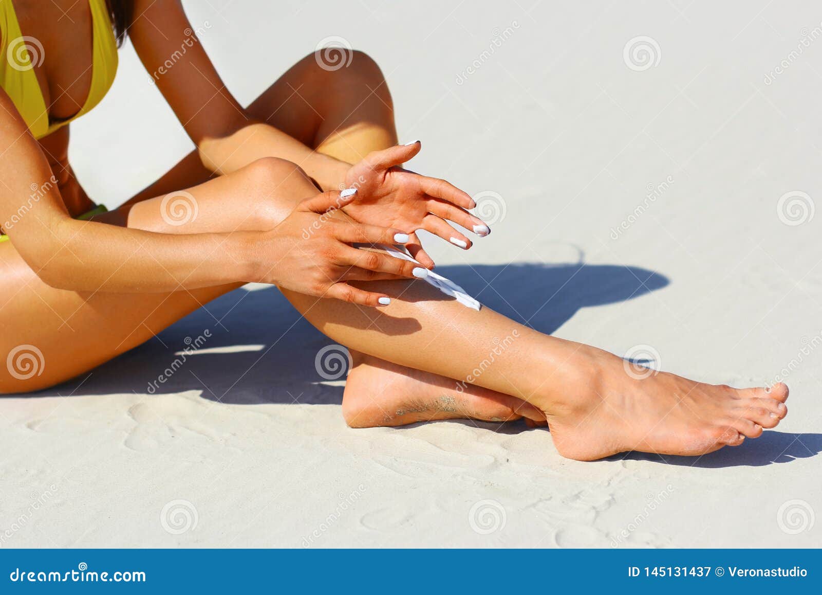 woman`s beautiful legs on the beach. tan woman applying sunscreen on legs. close-up