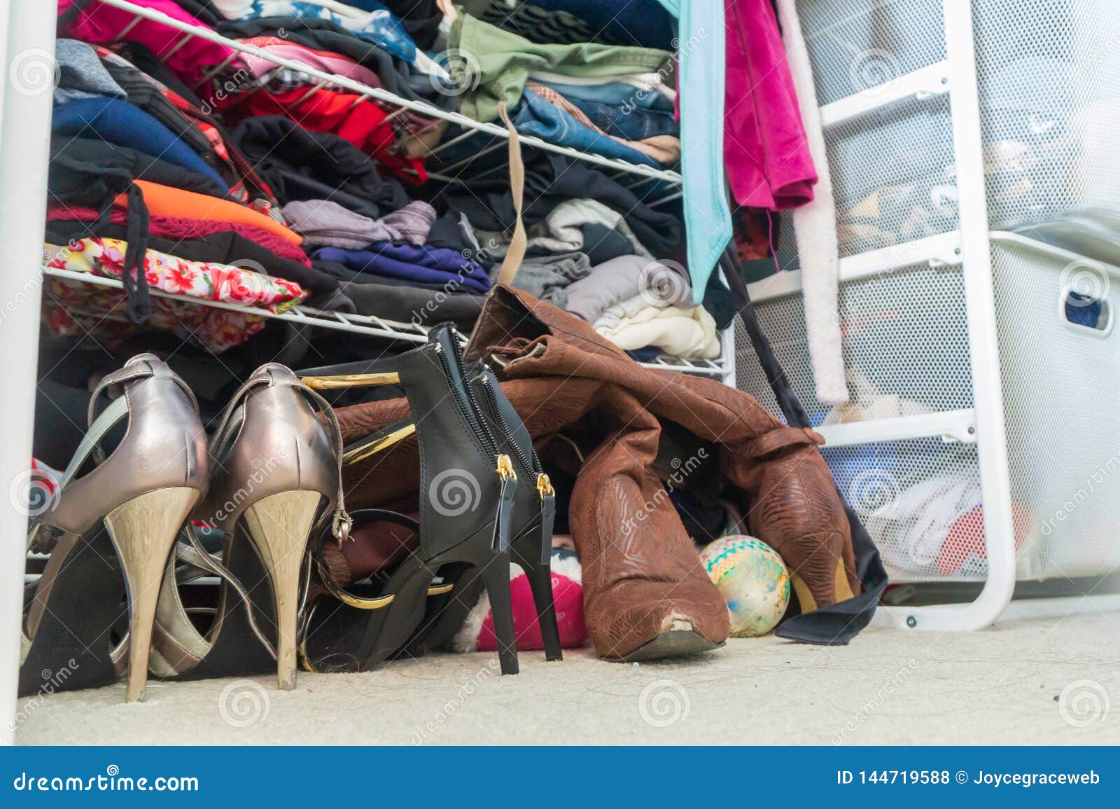 woman`s closet with high heel shoes, stacked, folded clothes on shelves and part of robes hanging. depicting closet organization,
