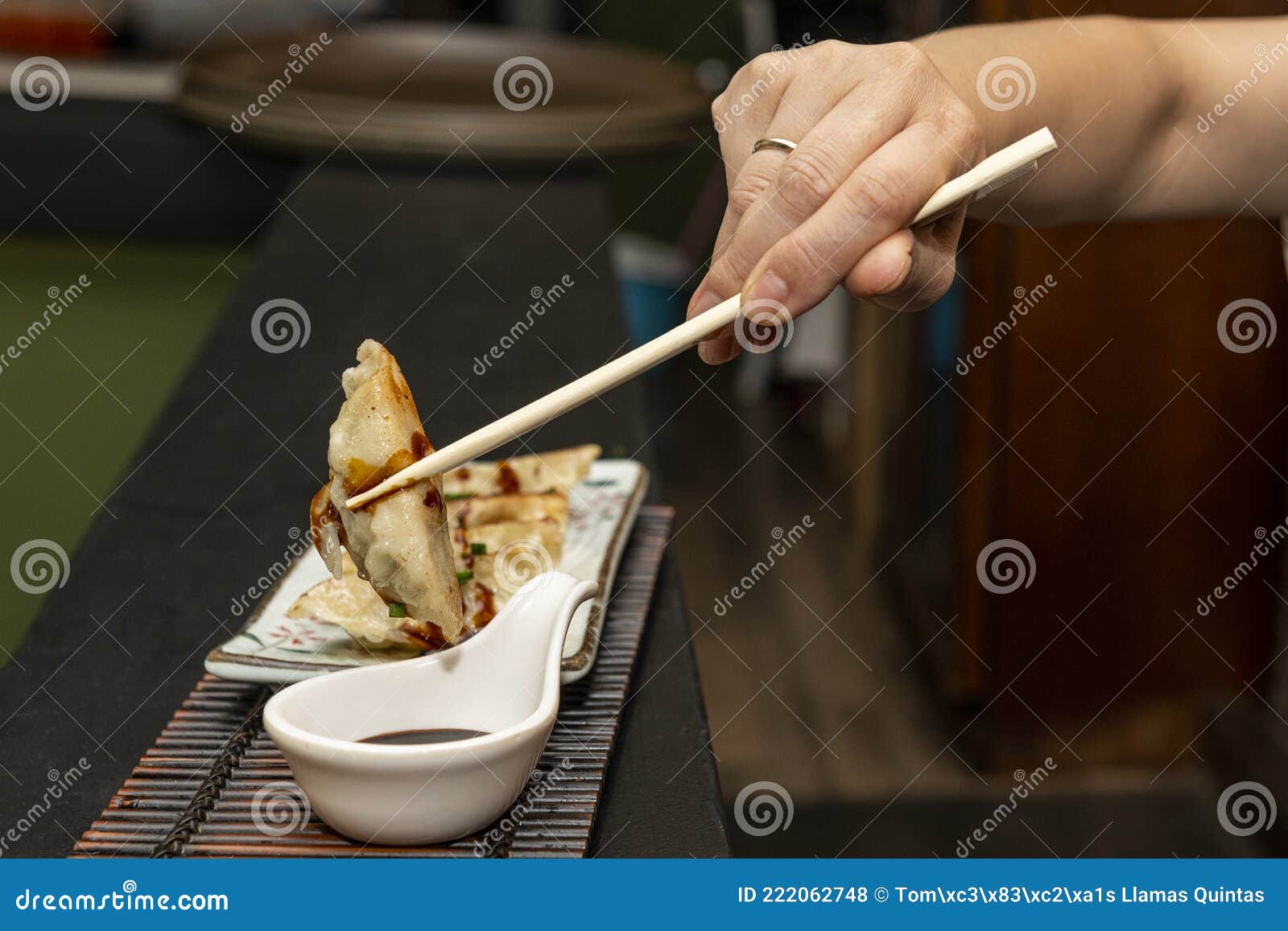 woman's hand with chopsticks dipping a gyoza in soy sauce and then gobbling it up with delight