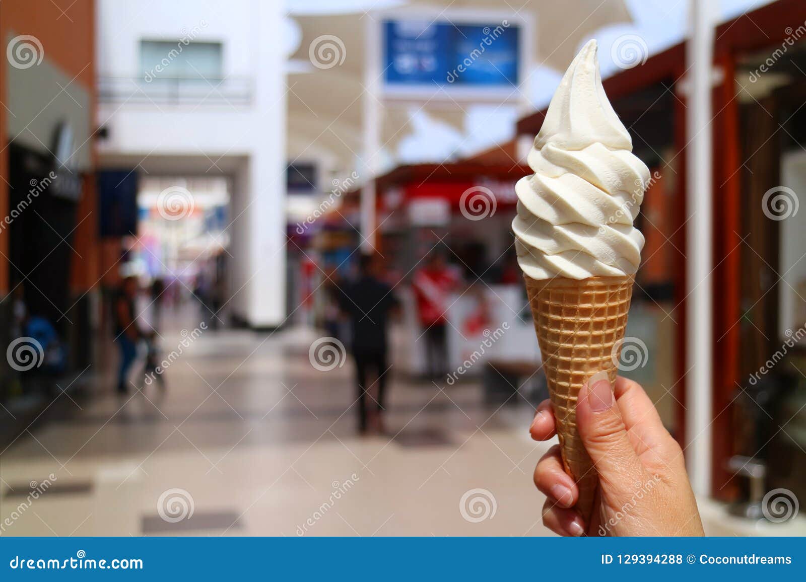 woman`s hand holding vanilla milk soft serve ice cream cone in the sunlight