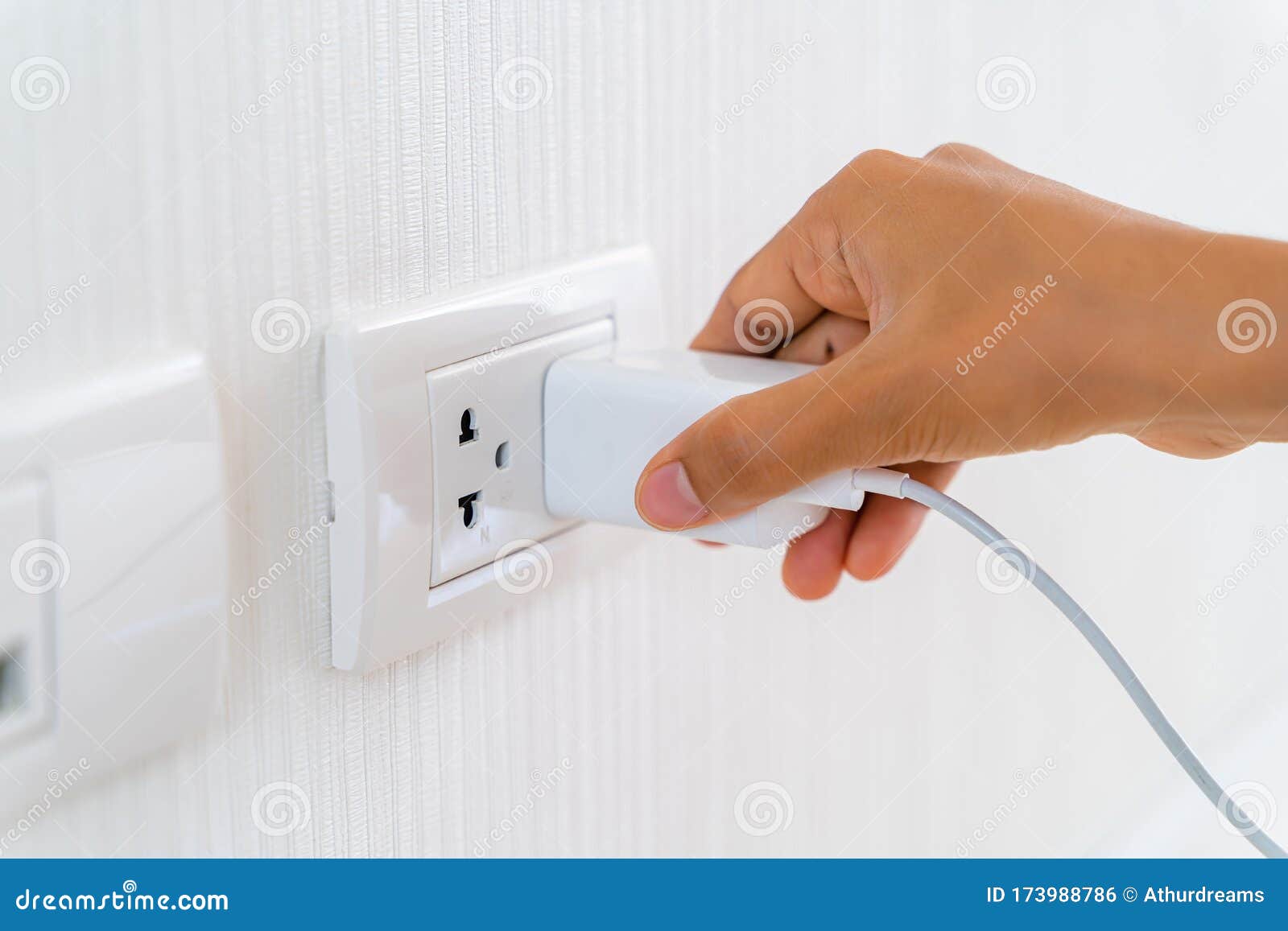 woman`s hand inserting electrical power cord plug into receptacle on wall outlet