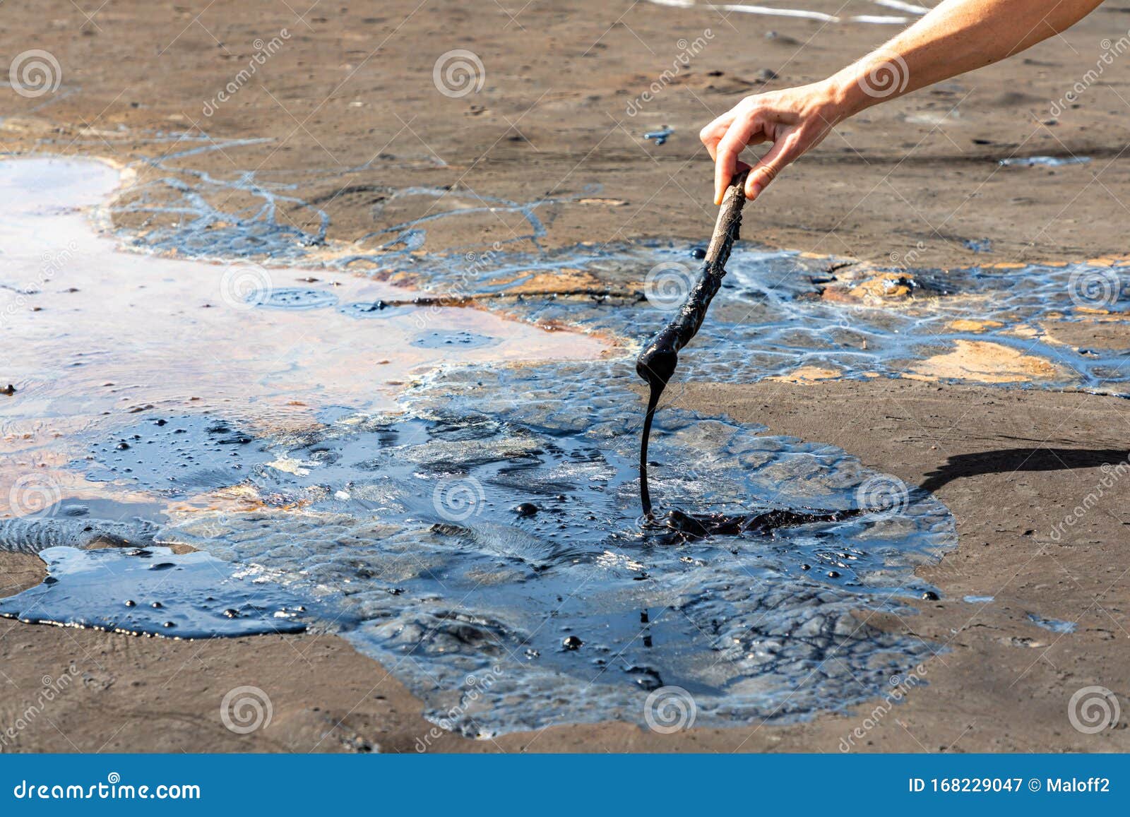 a woman`s hand stirring liquid asphalt with a wooden stick at pitch lake, la brea, trinidad island, trinidad and tobago
