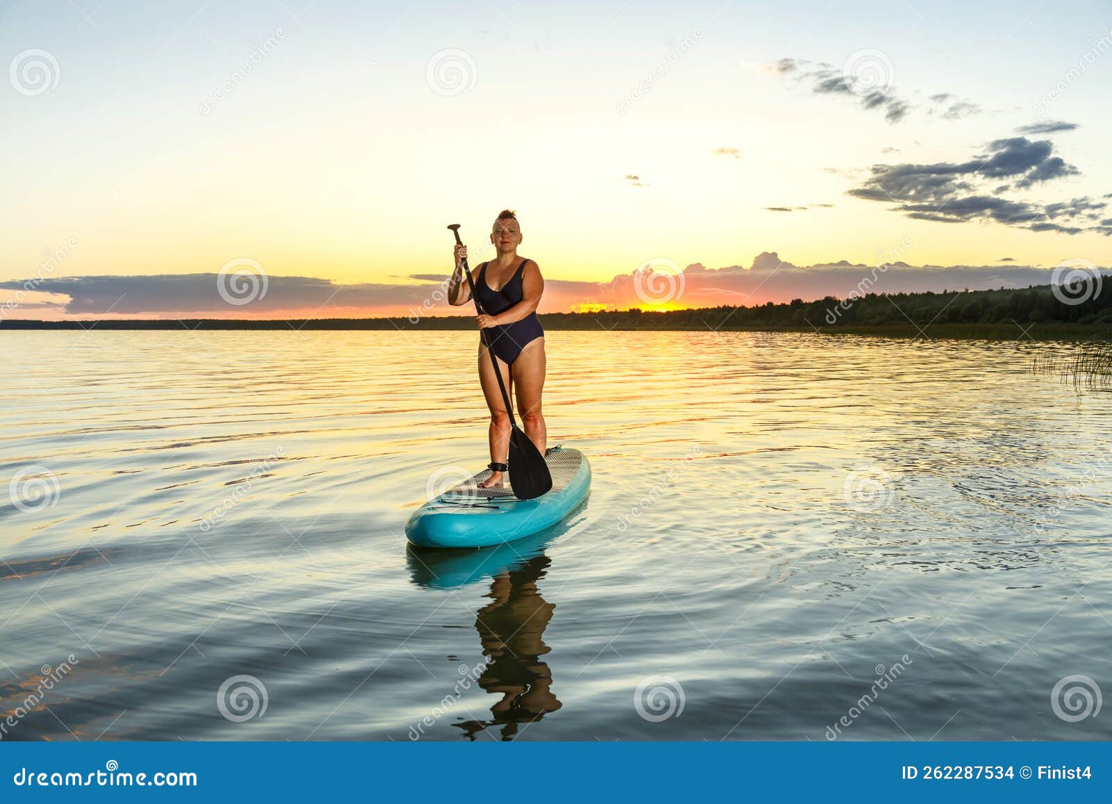 A Woman in a Shaved Swimsuit with a Mohawk on a Sup Board at Sunset in ...